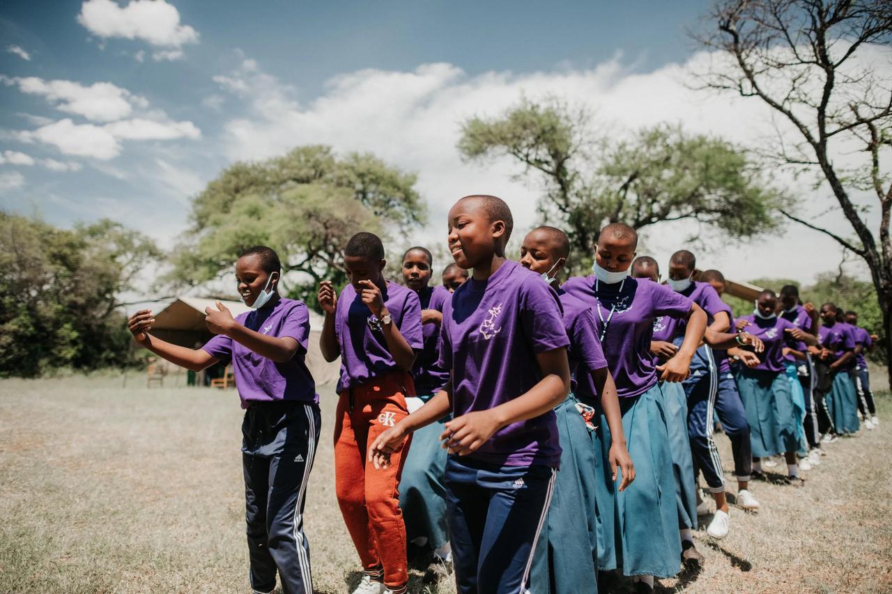 Schoolgirls in team shirts stride through the bush in a laughing line
