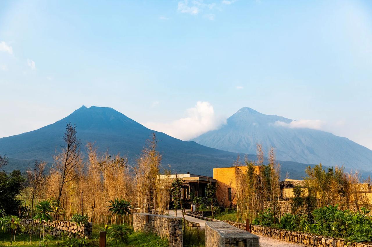 A lodge sits beneath the Virunga volcanoes in golden light