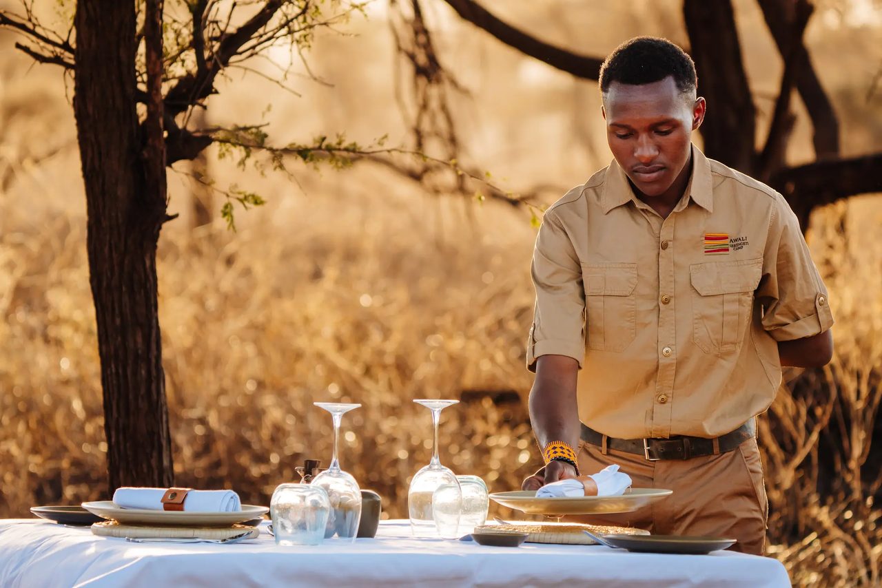 Sail camp host setting a private bush table at golden hour