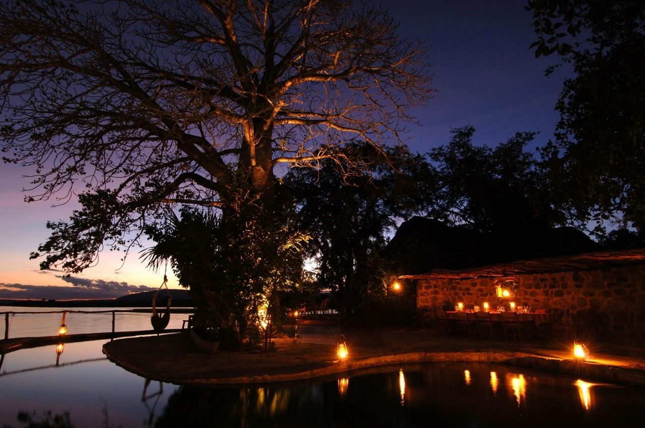 A southern Tanzania camp lit by lanterns at dusk beside the water