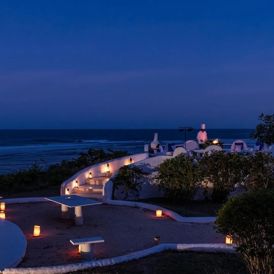 A coastal terrace at dusk with lanterns and the Indian Ocean beyond