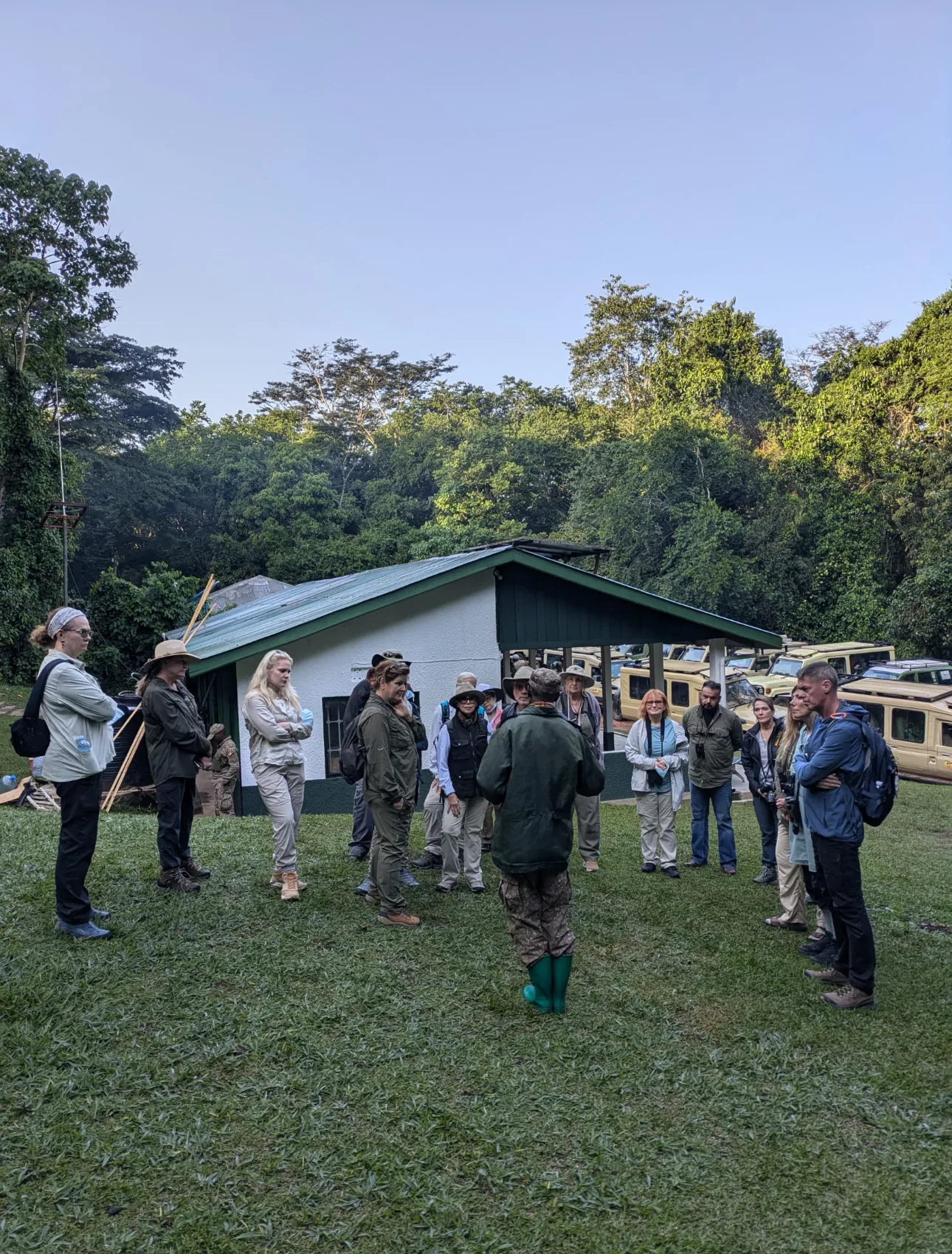 Trekkers in rain jackets sit in a circle on the forest floor while a ranger briefs them before a Bwindi gorilla trek