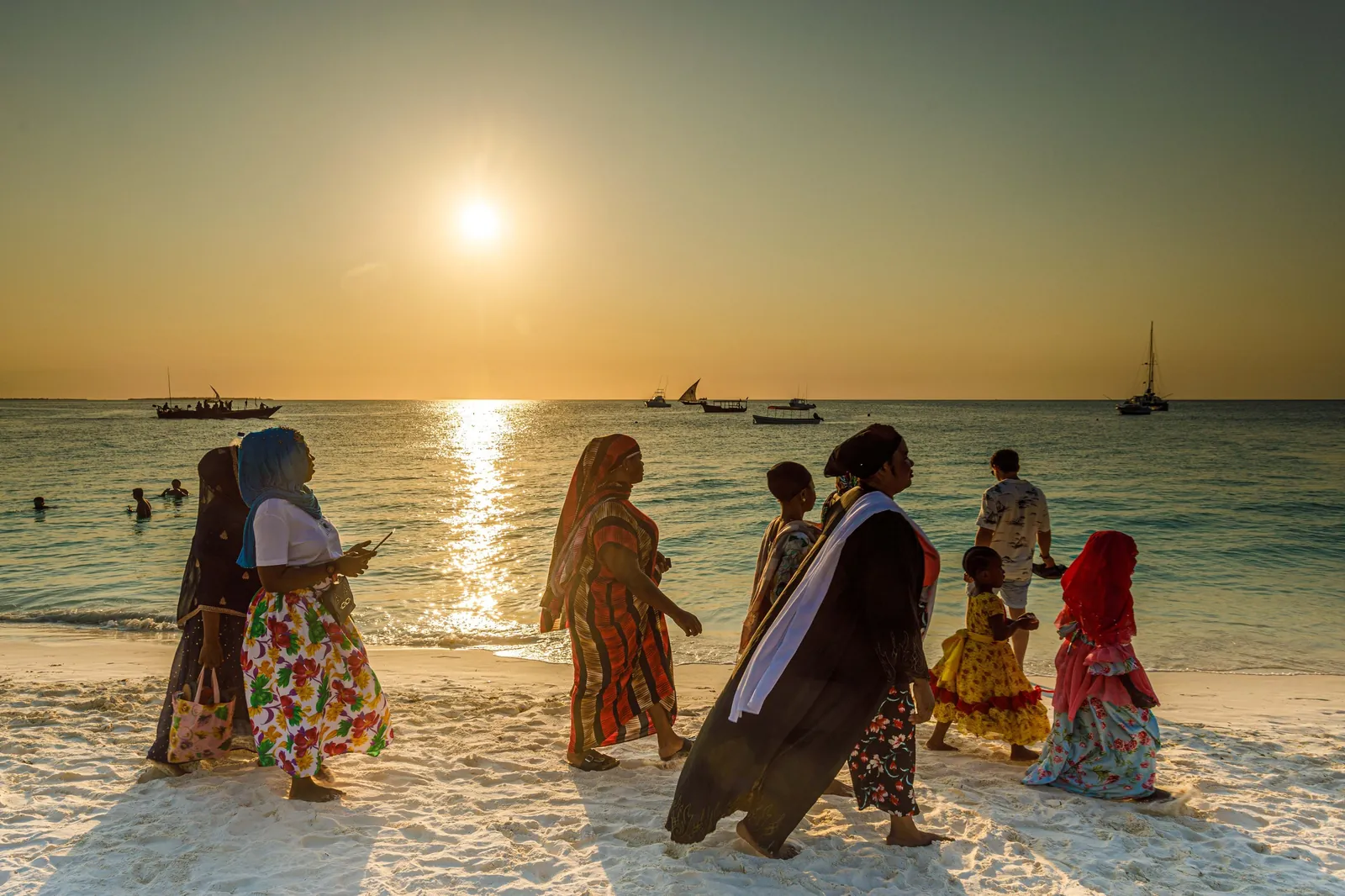 Women in bright dress walk the surf line of the coast