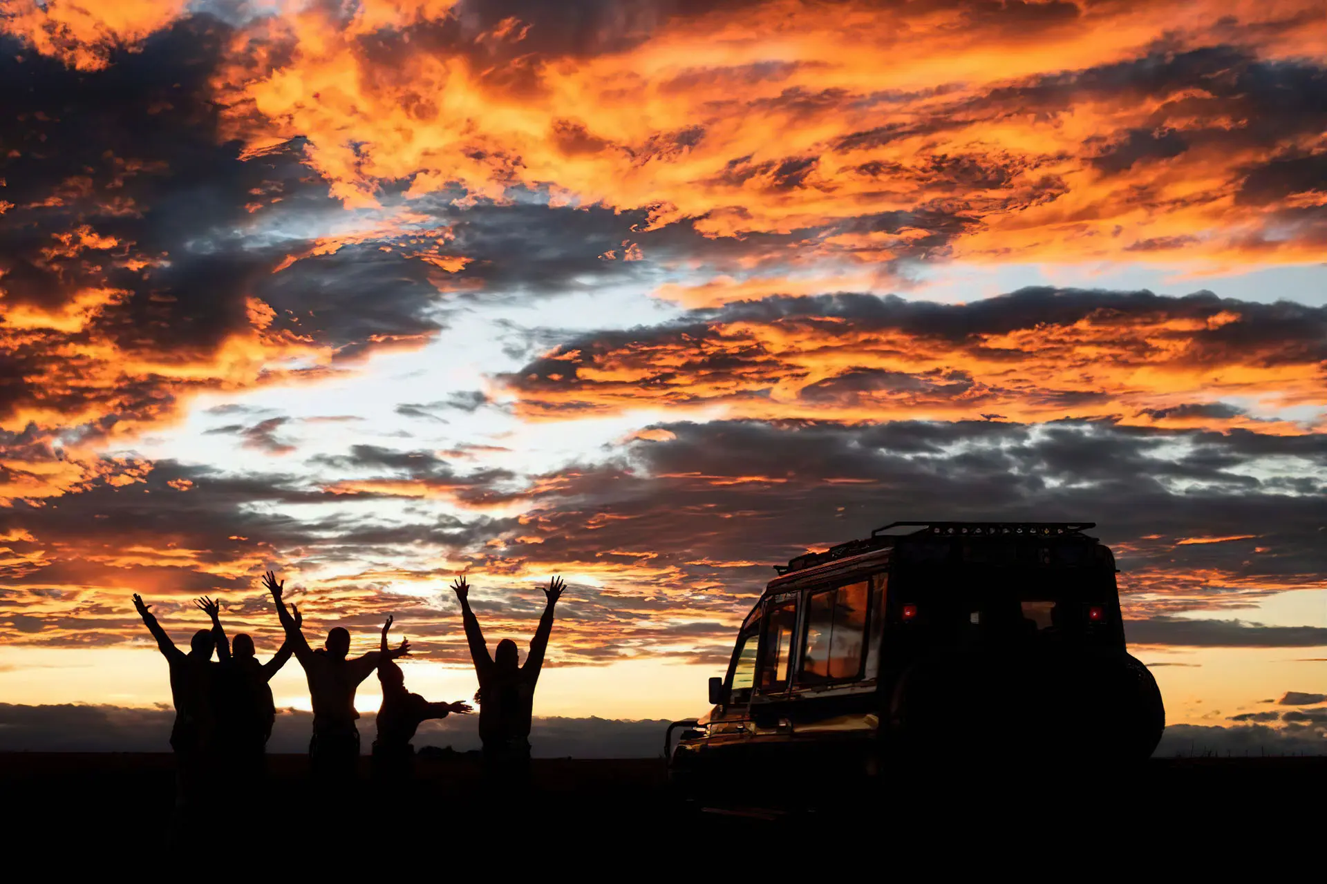 Sail safari team and vehicle silhouetted beneath an East African sunset