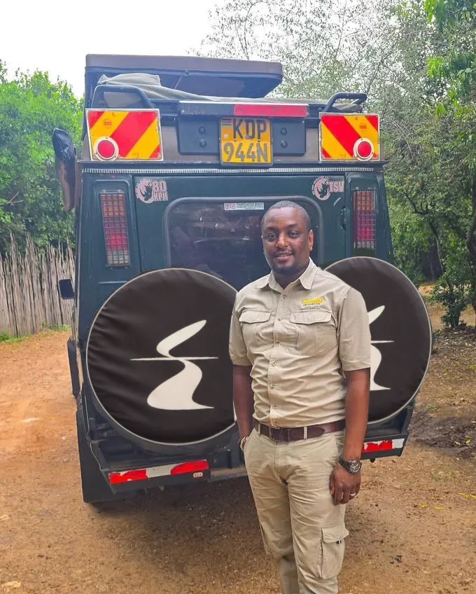 A Kenya head guide in safari clothing stands beside a Sail Safaris DMC vehicle in the Maasai Mara