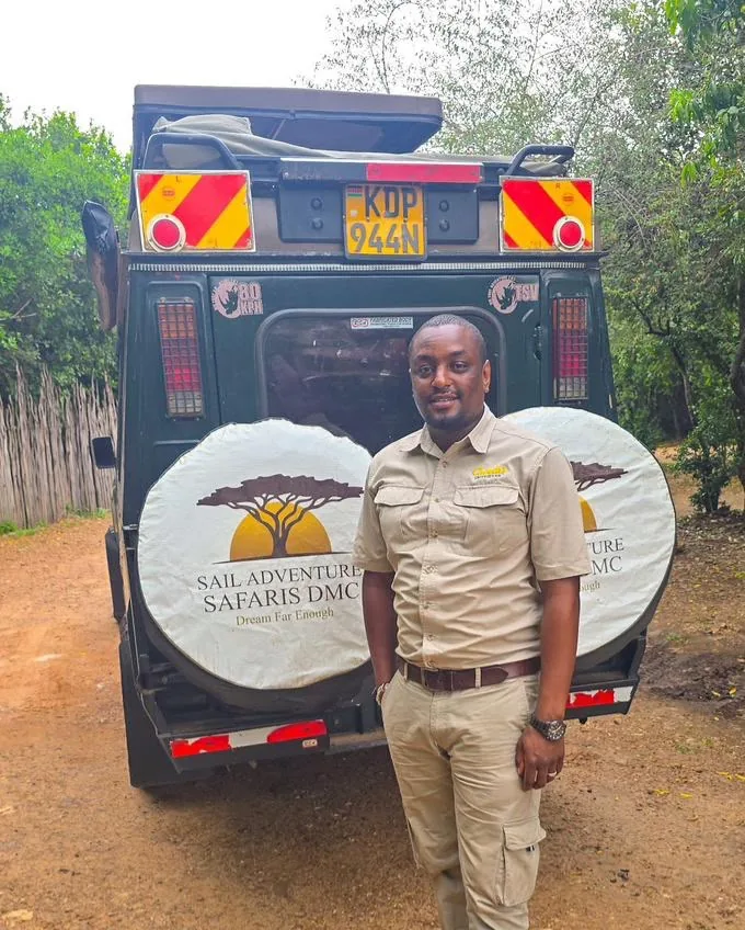 A Kenya head guide in safari clothing stands beside a Sail Safaris DMC vehicle in the Maasai Mara
