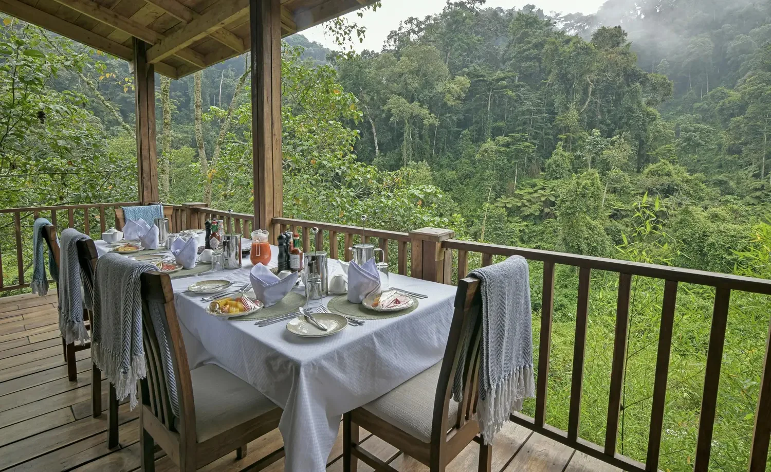 A long table waits on a forest lodge verandah