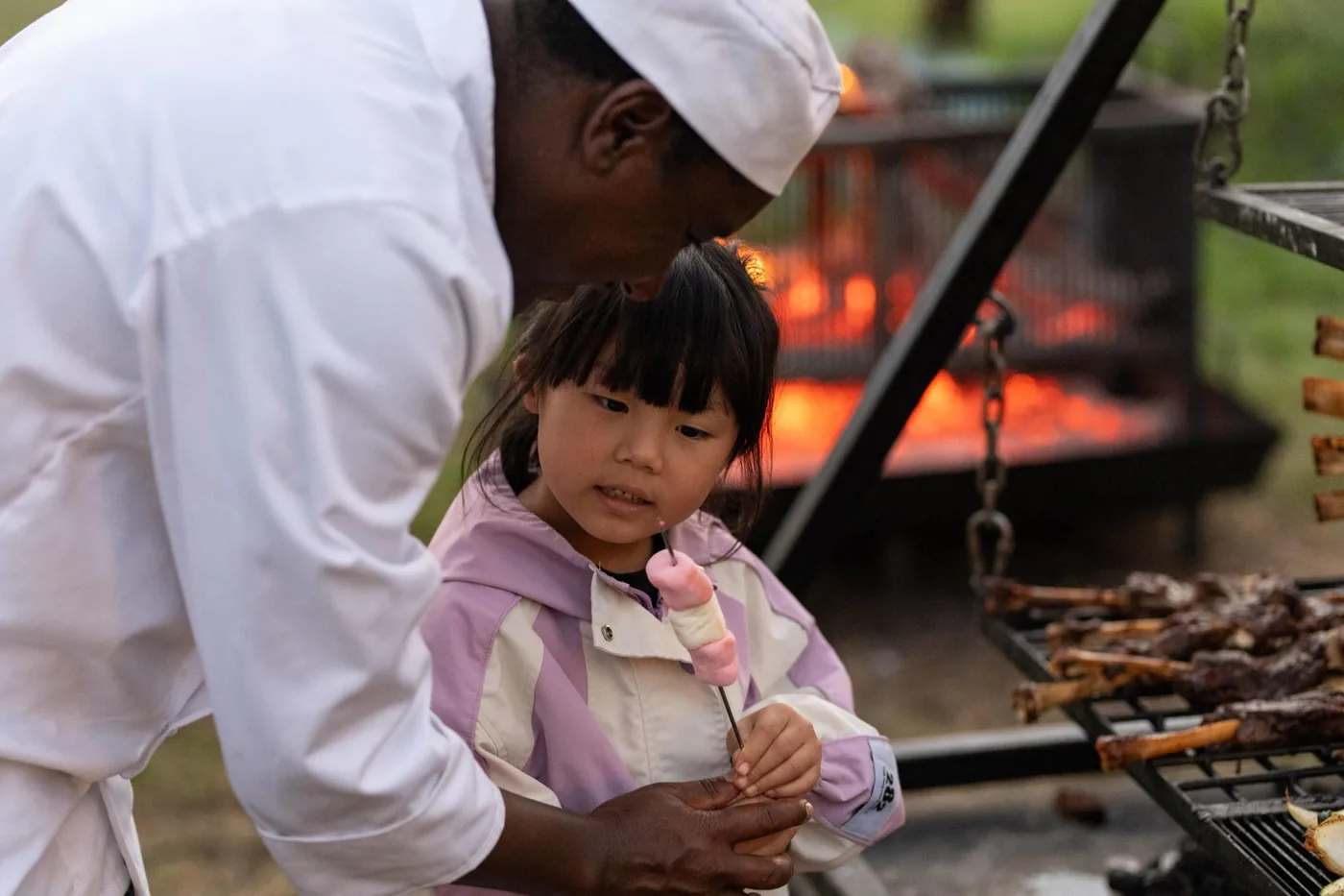 A child stands with a camp chef beside the boma fire