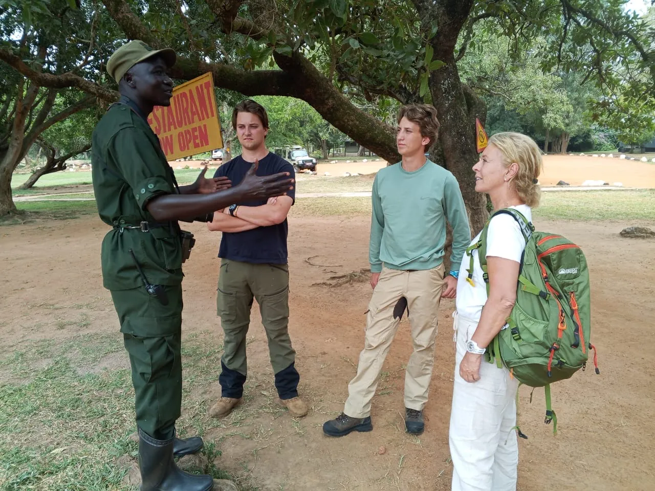 A ranger briefs a small trekking party at a forest edge before they walk in, guests standing with daypacks.