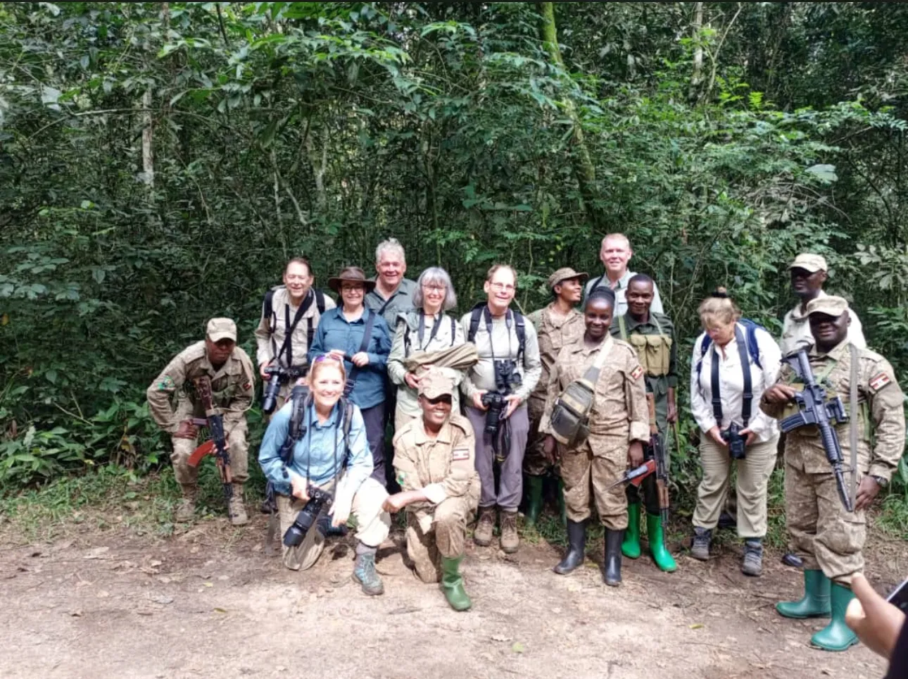 A trekking party gathers at a forest edge with rangers and porters, ready to walk in as a group.