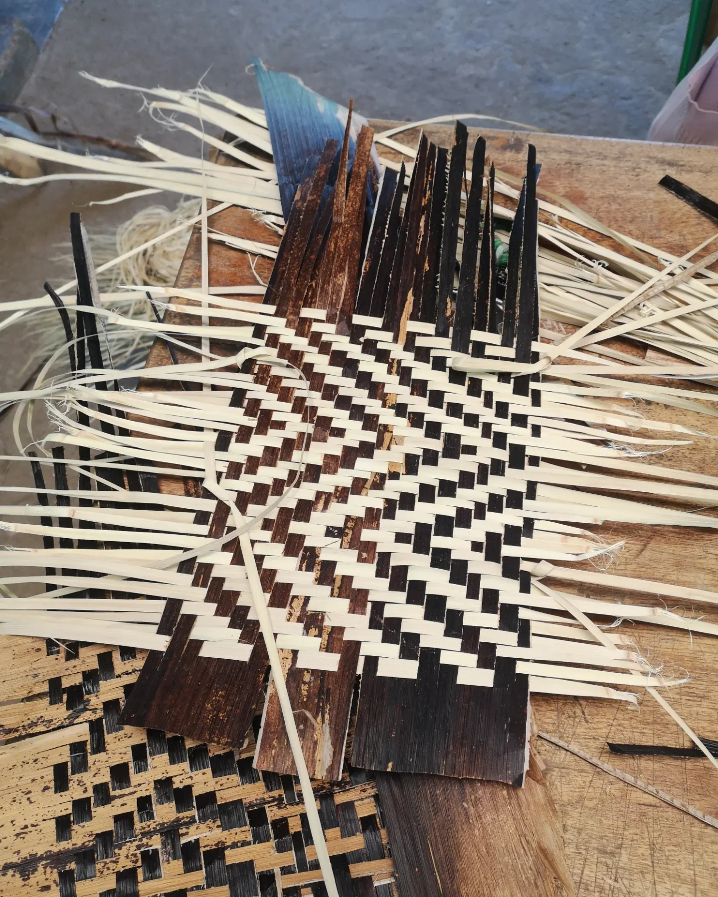 Hands weave a black and white pattern into a basket