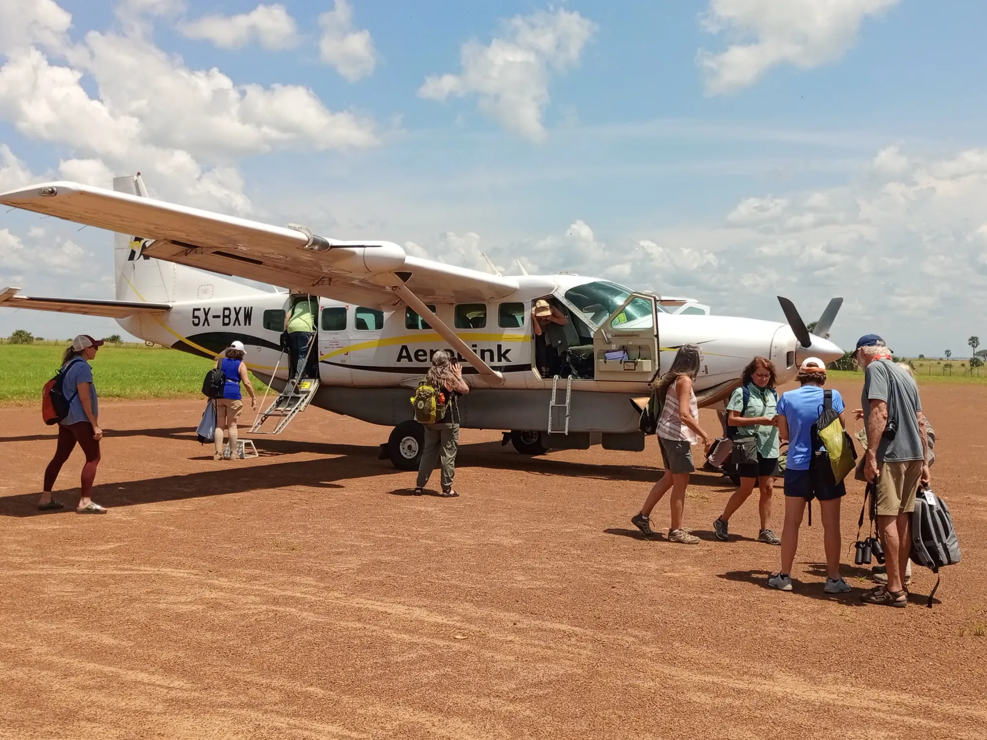 Guests walk toward a white Aerolink Cessna Caravan on a grass bush airstrip, ready for a domestic transfer.