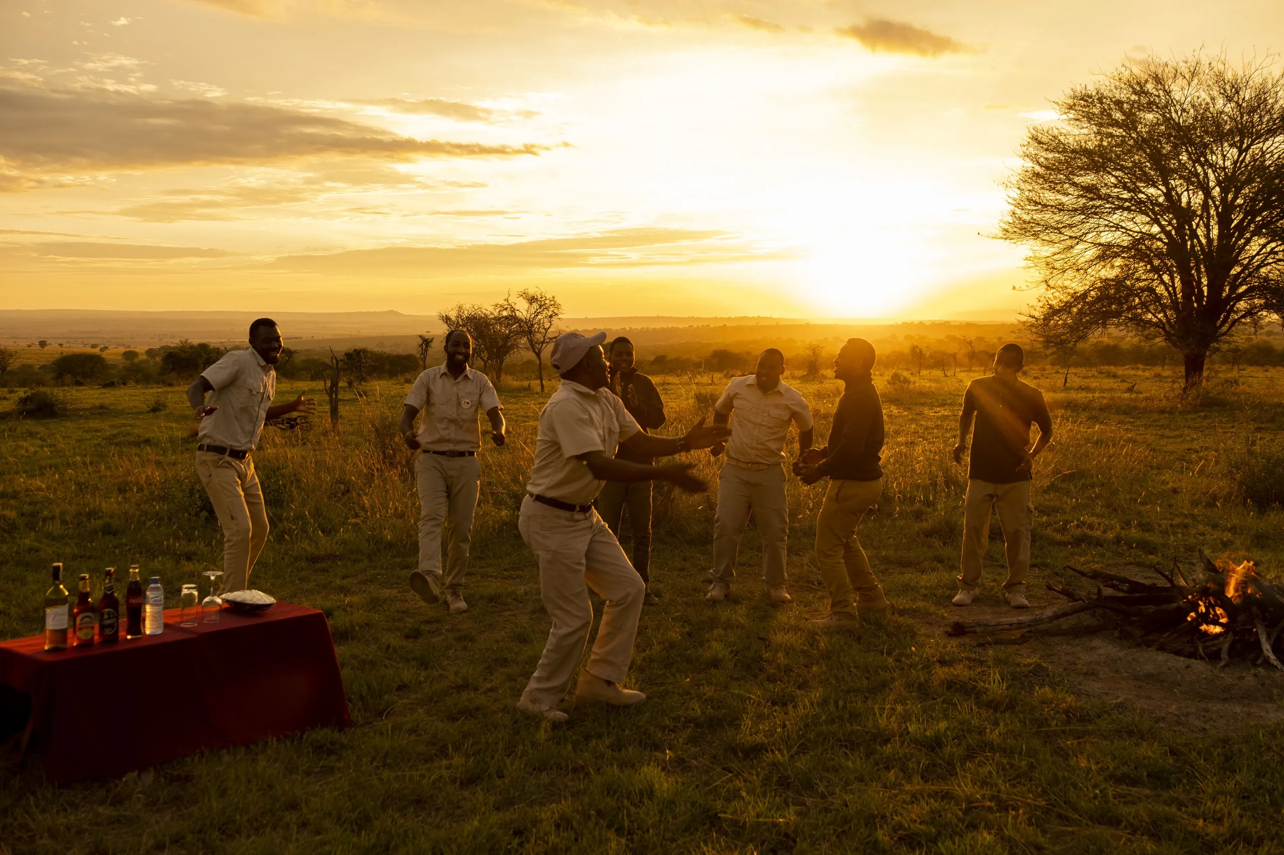 Camp staff gather in song around the sundowner fire at golden hour