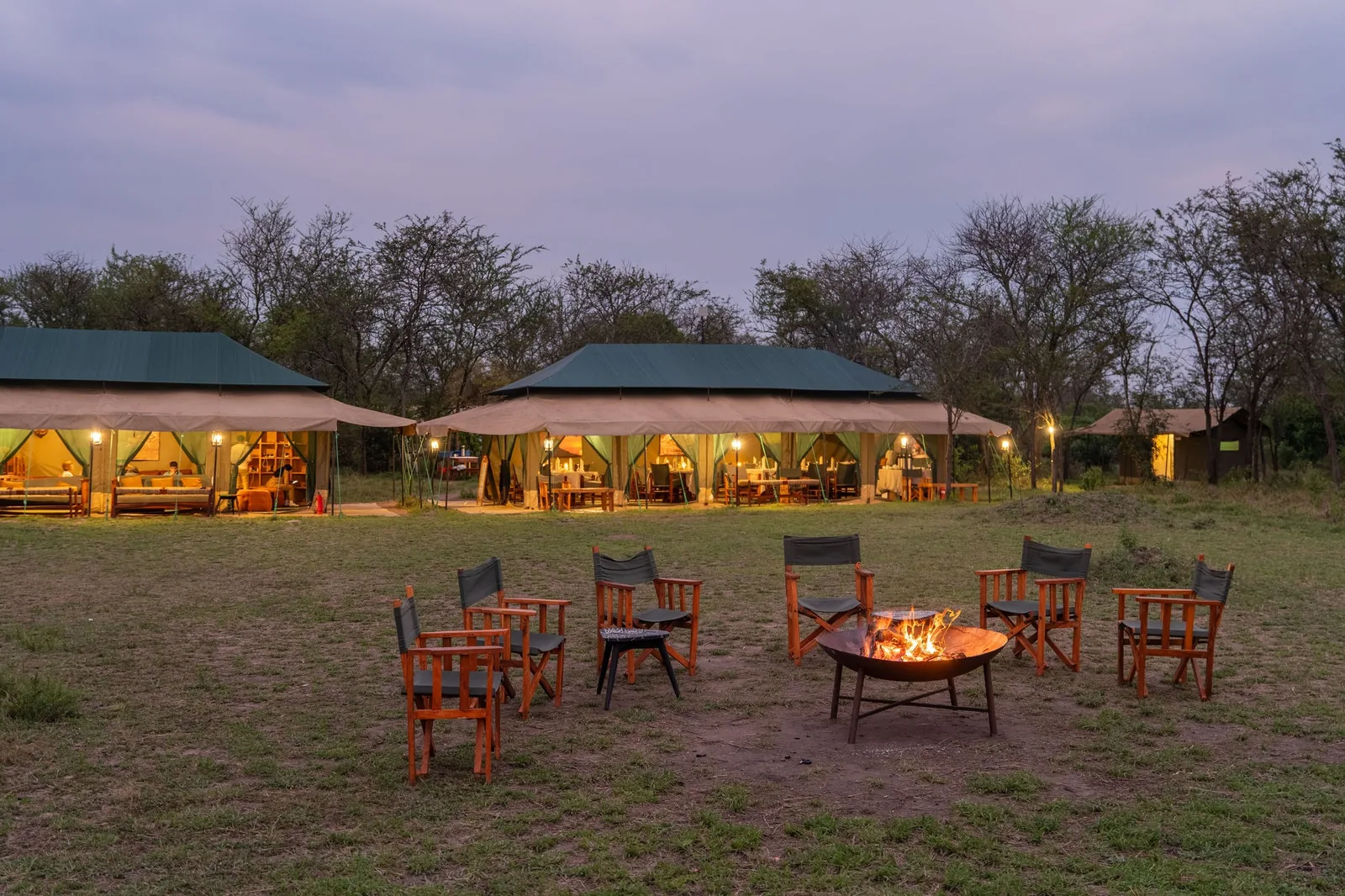 A seasonal camp glows at dusk around its fire