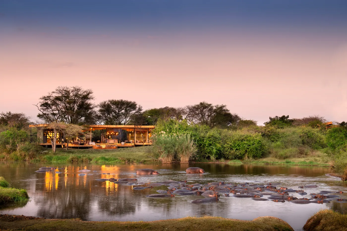 A lodge sits above a hippo river at dusk
