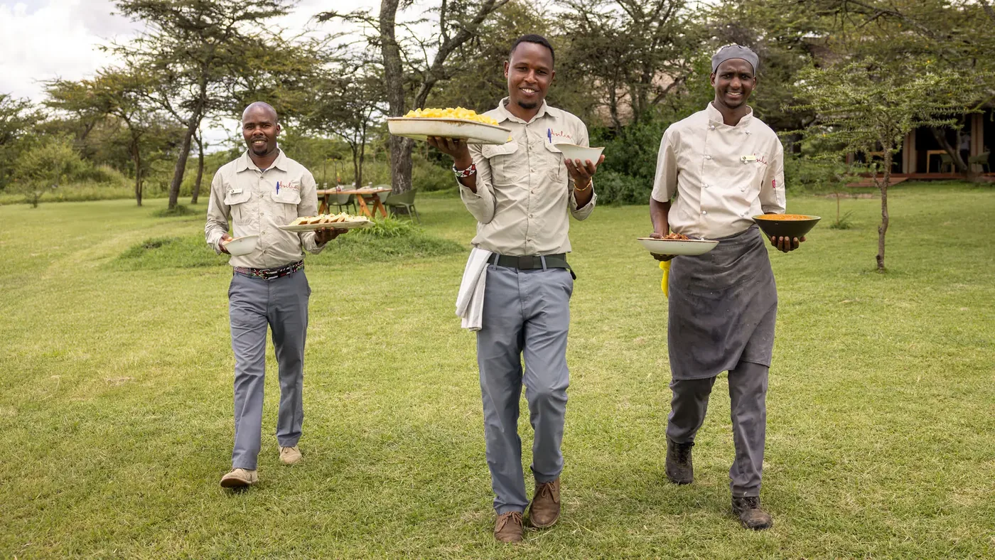 Camp staff in uniform stand with welcome trays at a Naboisho conservancy camp