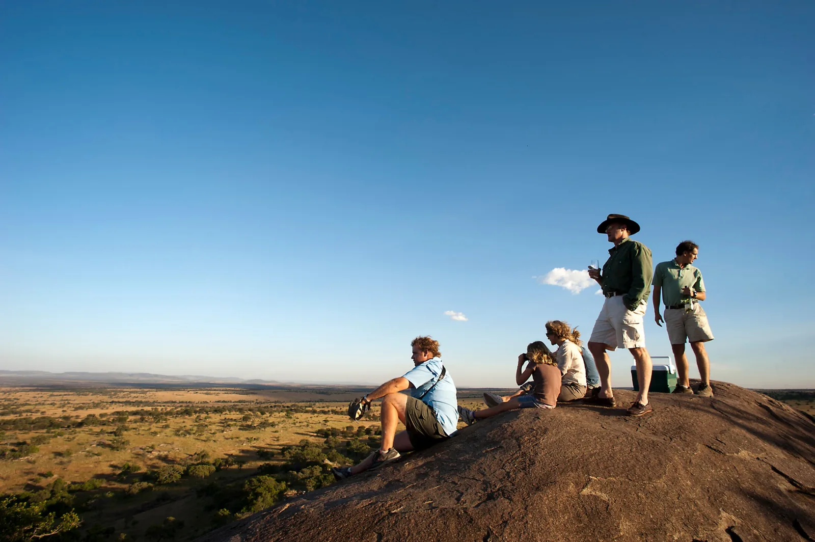 Guests stand with their guide on a rock above the evening plains
