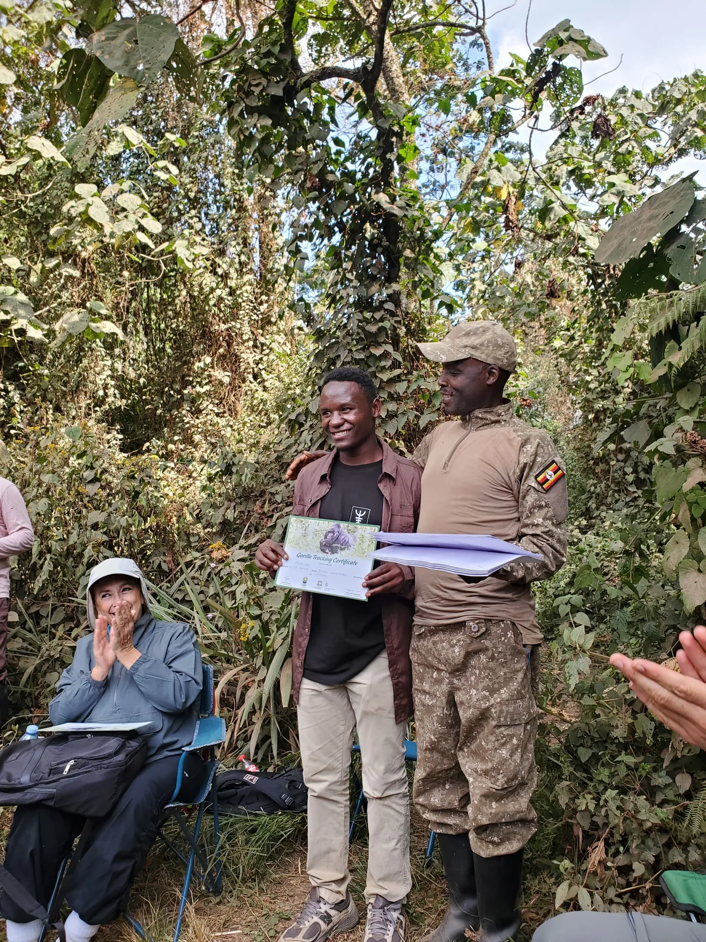 A guest in trekking clothes receives a gorilla-trek certificate from a UWA ranger after a Bwindi morning