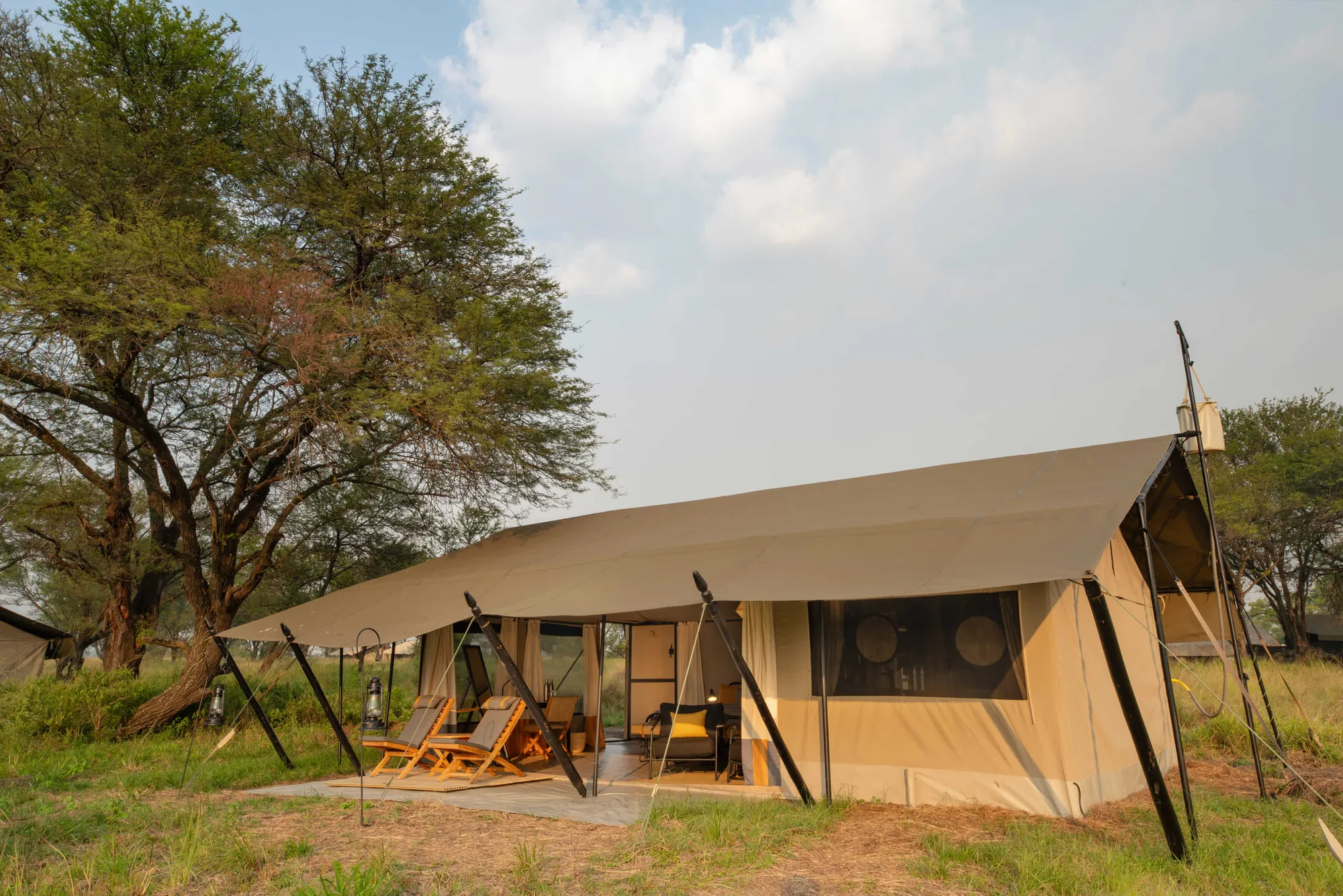 A guest tent sits in long grassland at Ubuntu Migration Camp, canvas and guy-ropes against an open sky.