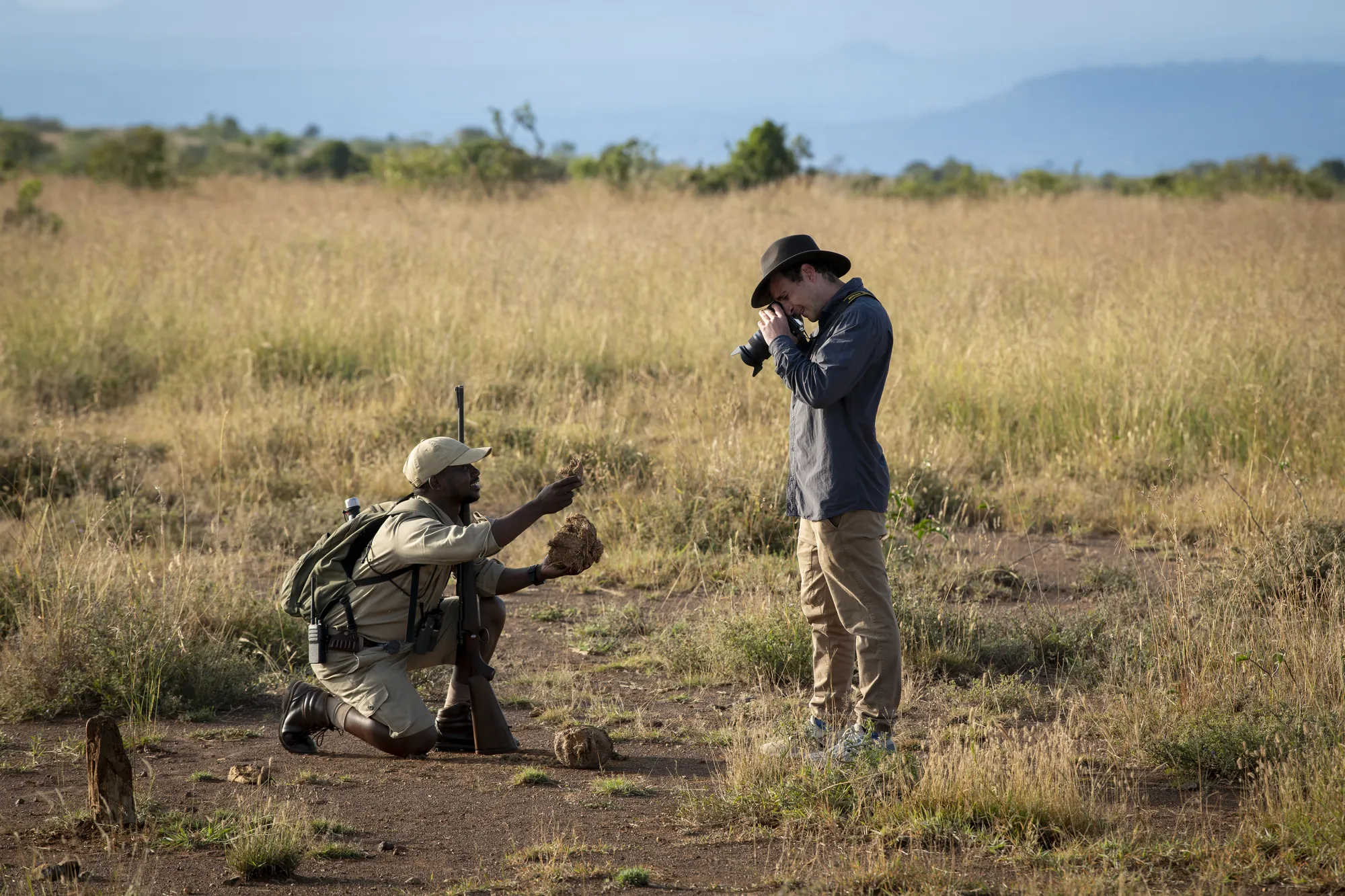 A walking-safari guide in khaki stands with two guests on open Laikipia grassland at Suyian Conservancy.