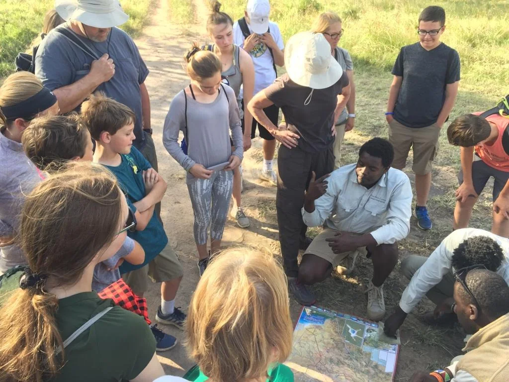 A guide crouches with a map, briefing a circle of attentive guests
