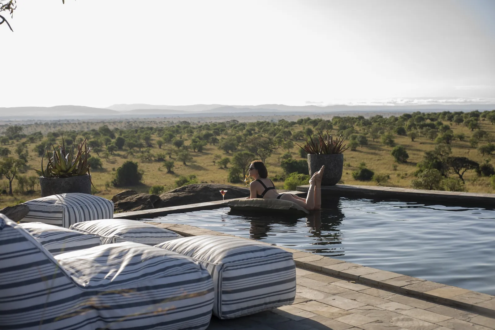 A couple rests at the pool's edge above the open plain