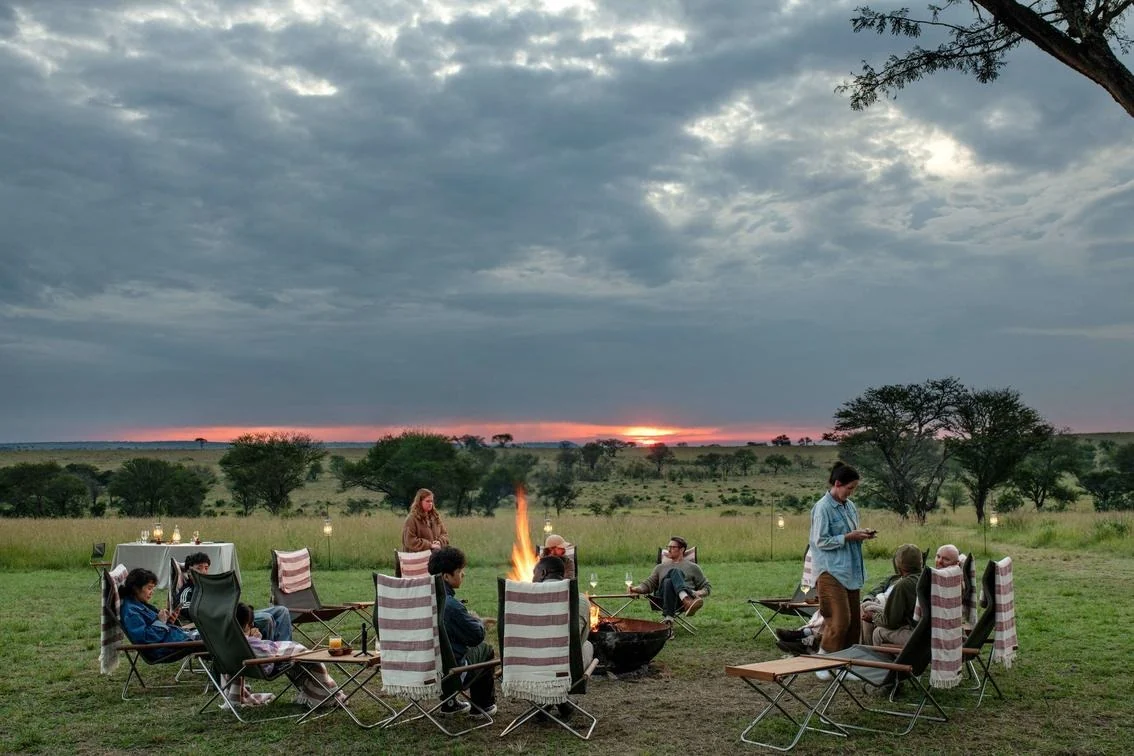 Guests settle at the firepit as the sun drops behind the kopjes
