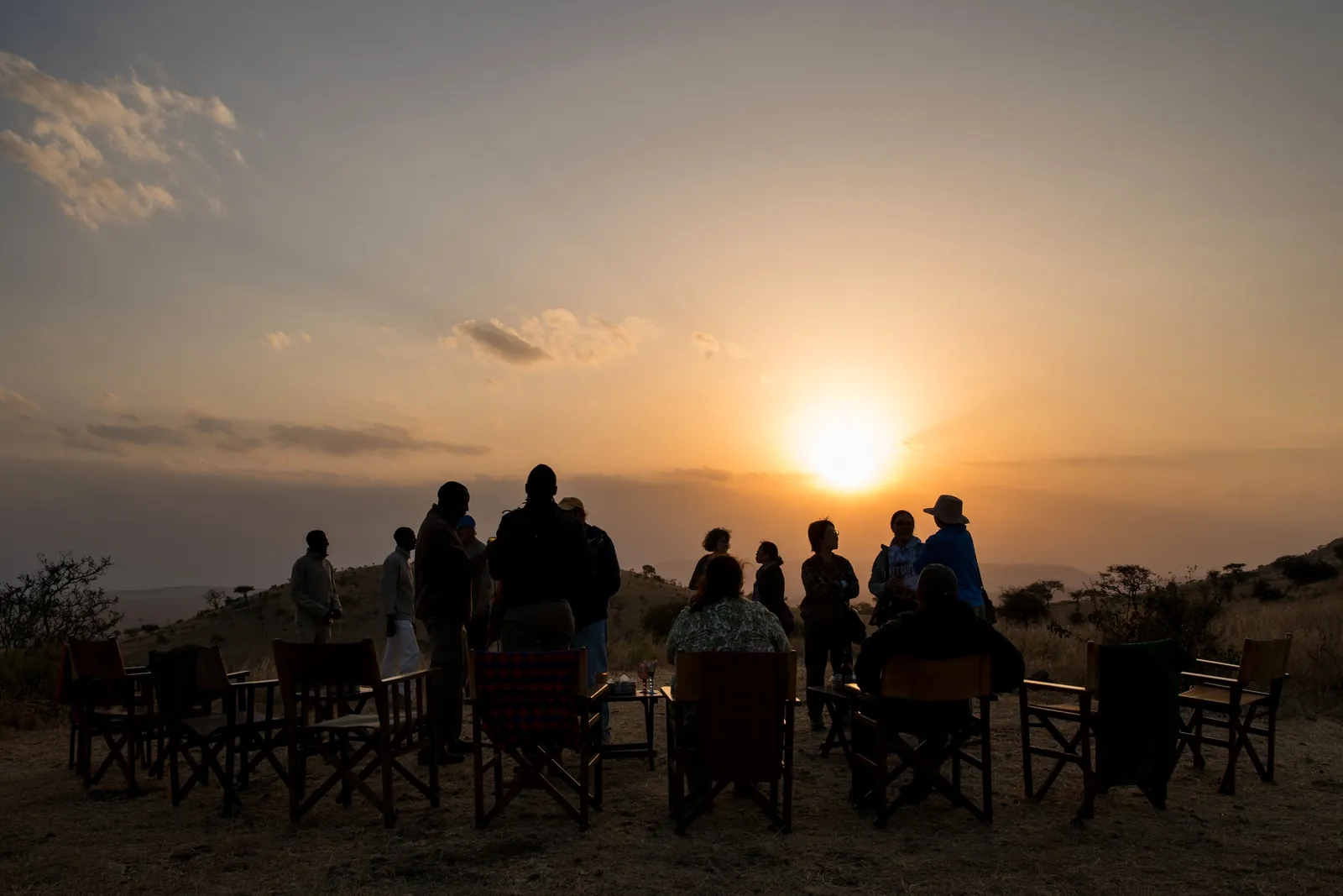 Guests settle into camp chairs as the sun drops over the plains