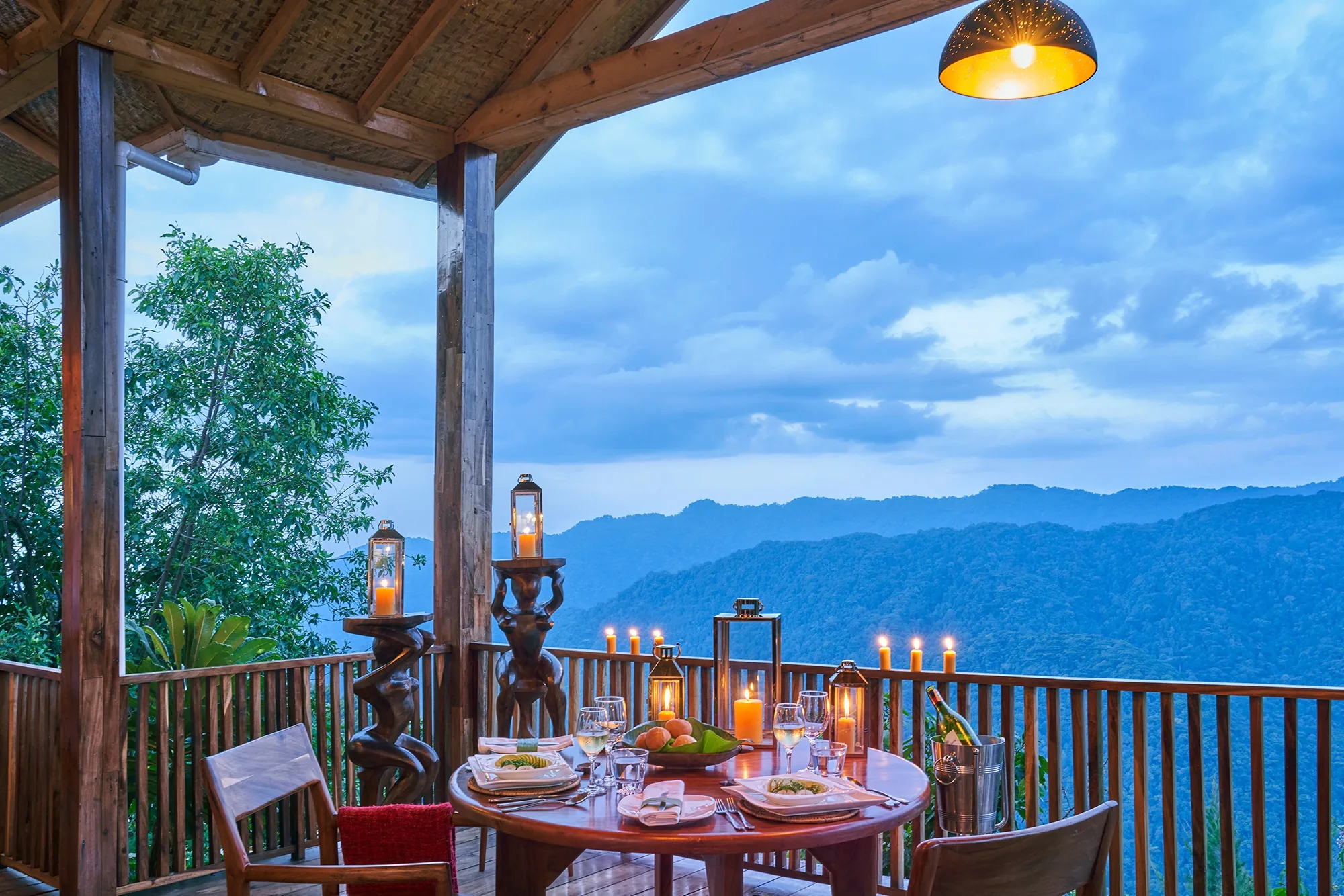 A dinner table set above blue ranges of evening hills