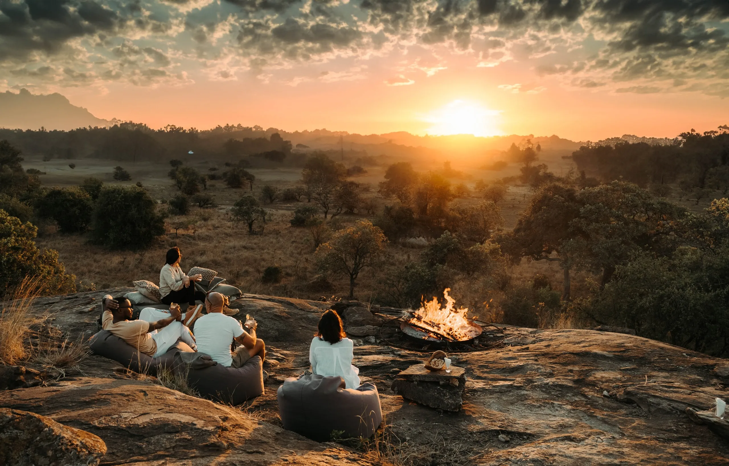 Guests gather at a firepit on the rocks as the sun drops