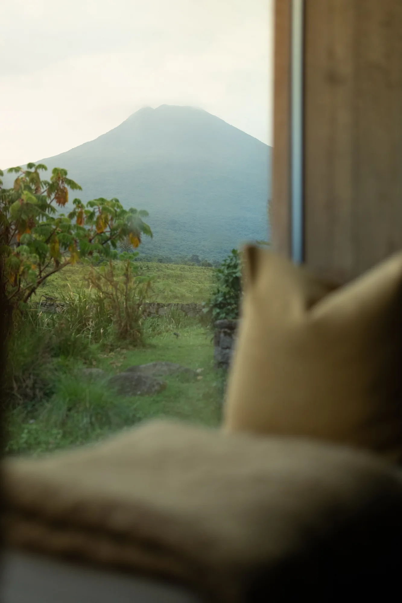A volcano fills the window of a quiet lodge suite in Rwanda