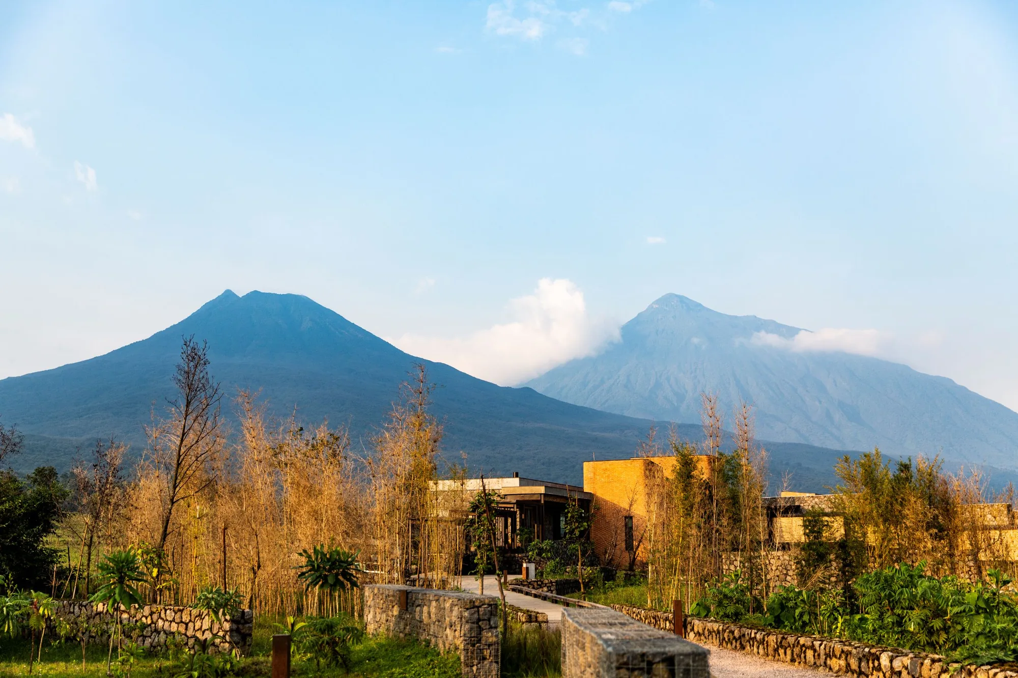 A lodge sits beneath the Virunga volcanoes in golden light