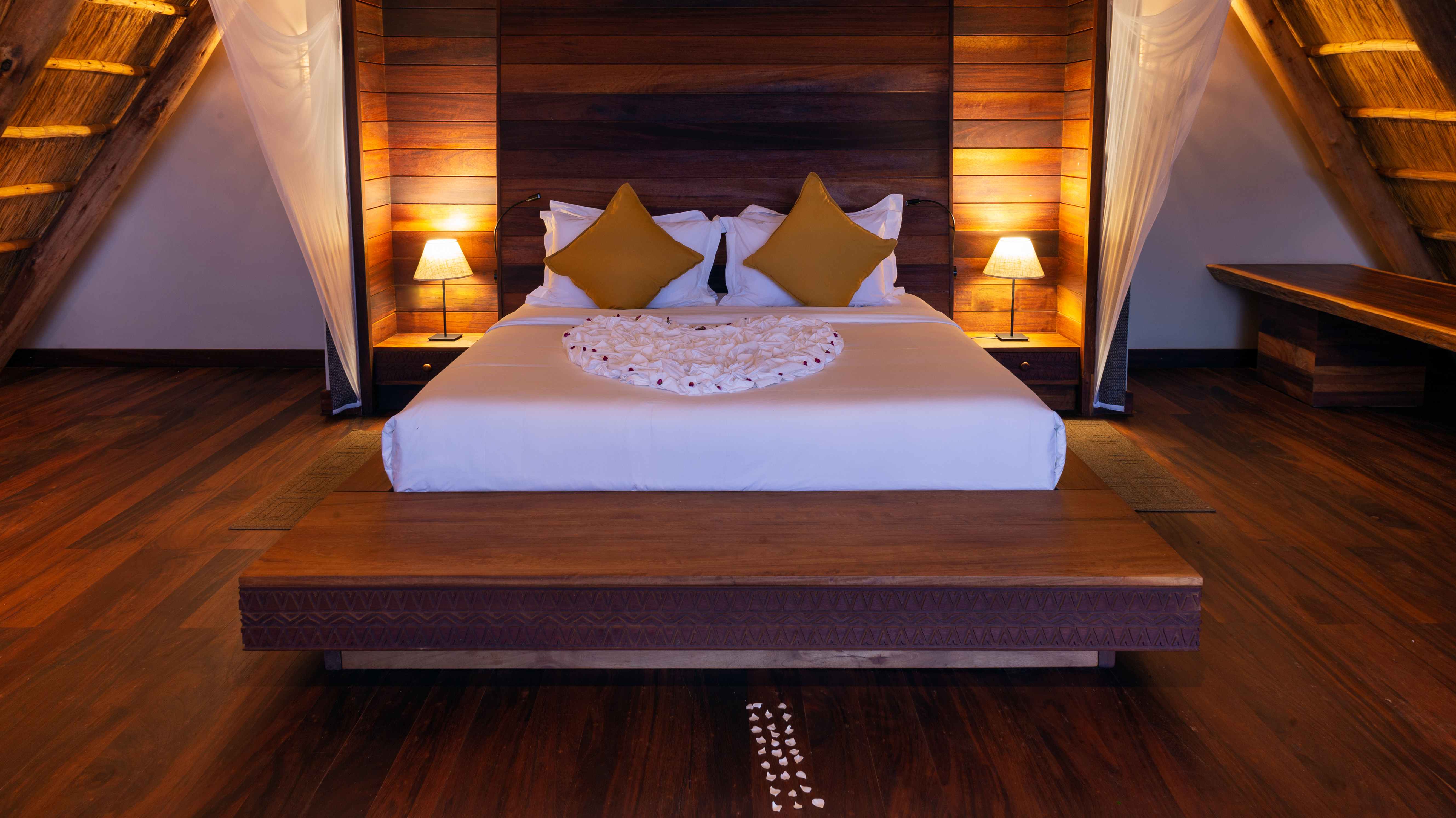 A bedroom at Nile Safari Lodge, the bed lit by lamps under a steep timber roof