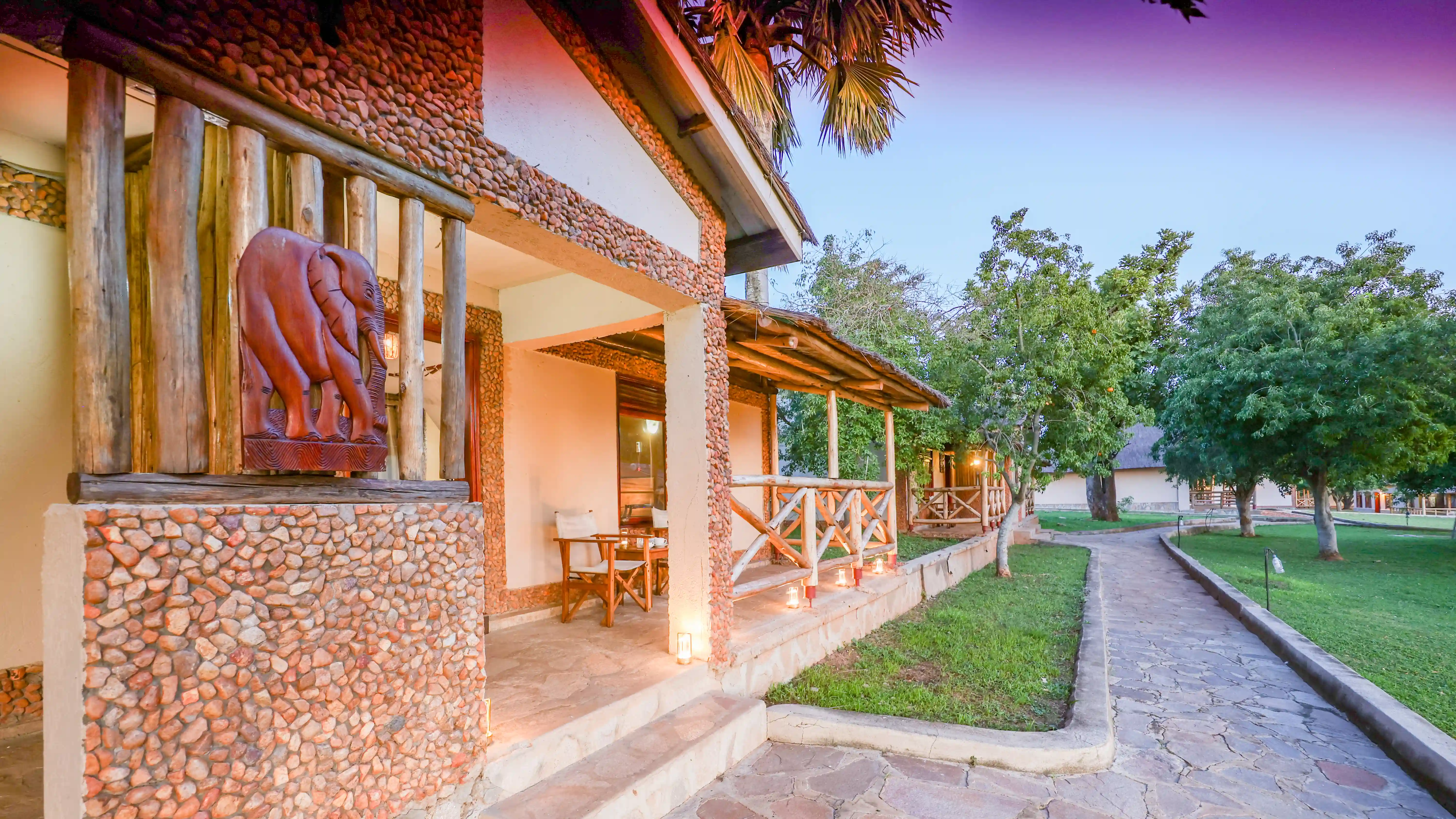 A cottage veranda at Pakuba Safari Lodge with a carved elephant, beside a stone garden path