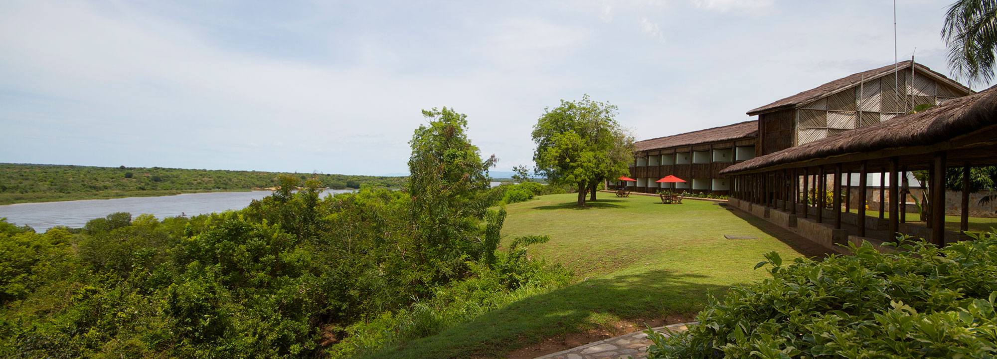 The thatched verandas of Paraa Safari Lodge above a sloping lawn, with the Nile and its wooded far bank to the left