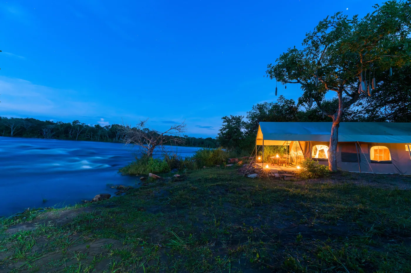 Safari tents glow at dusk beside the river