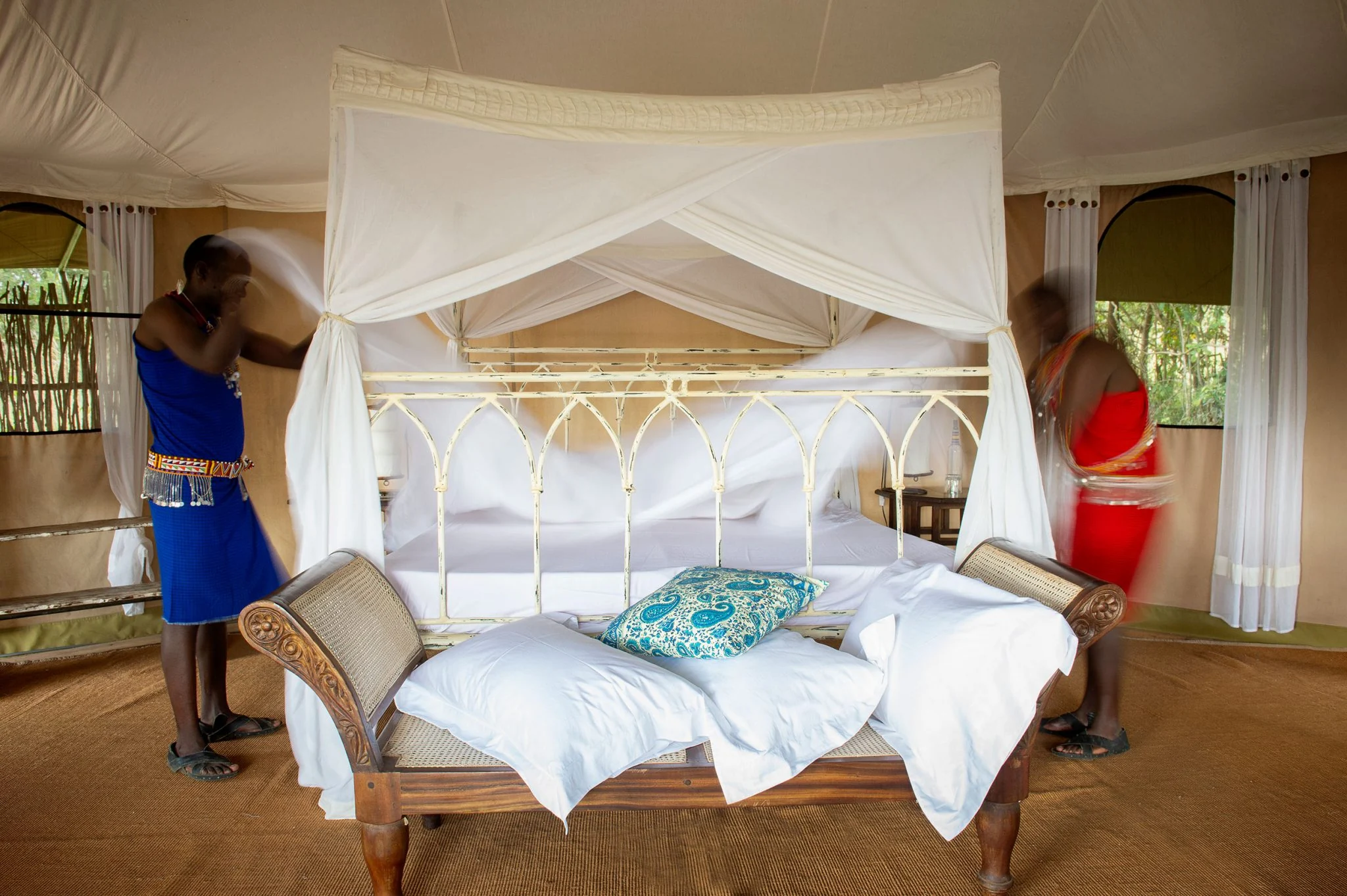 Camp staff making up a four-poster bed in a tent