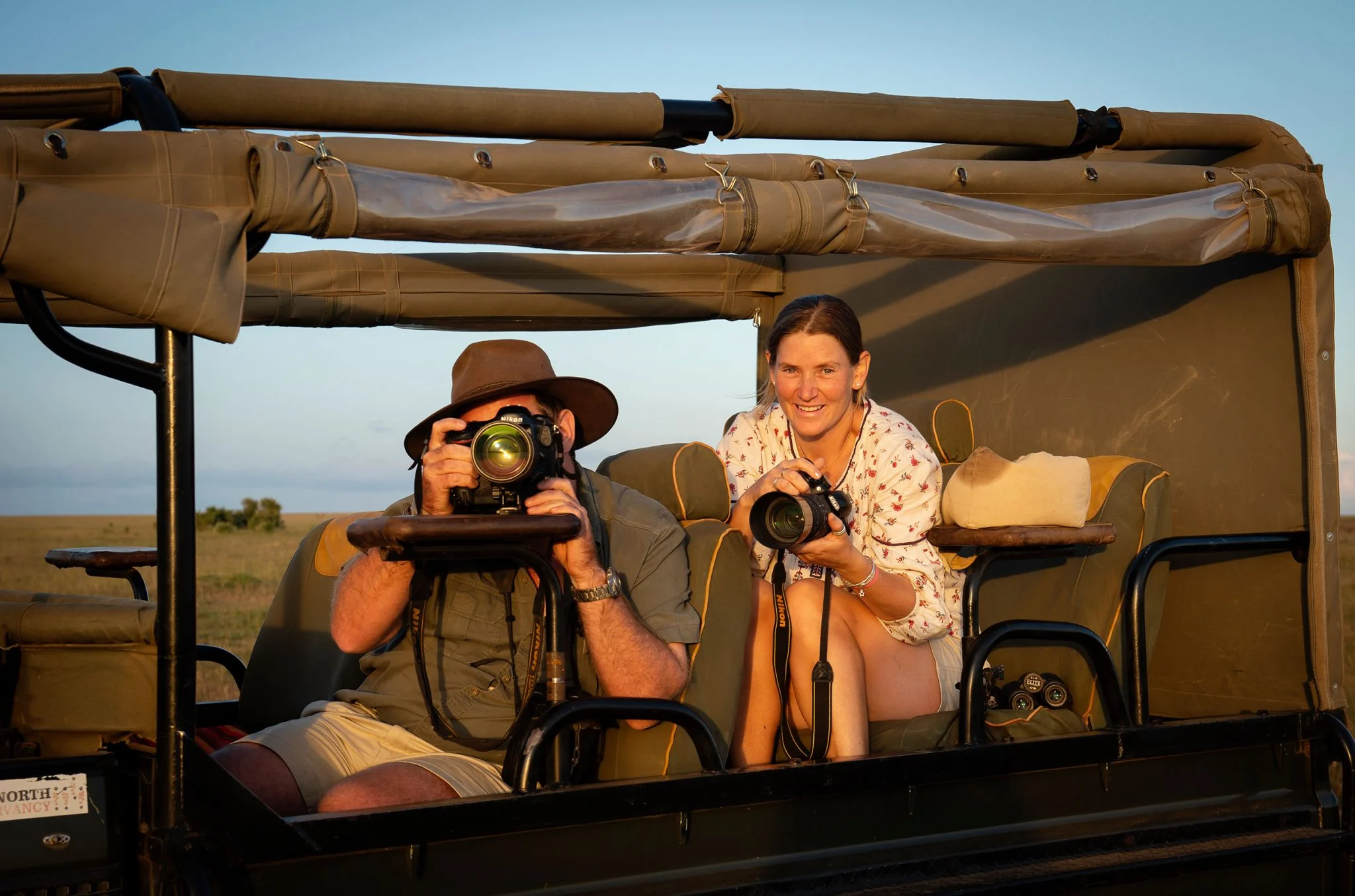 Two guests with cameras in an open safari vehicle