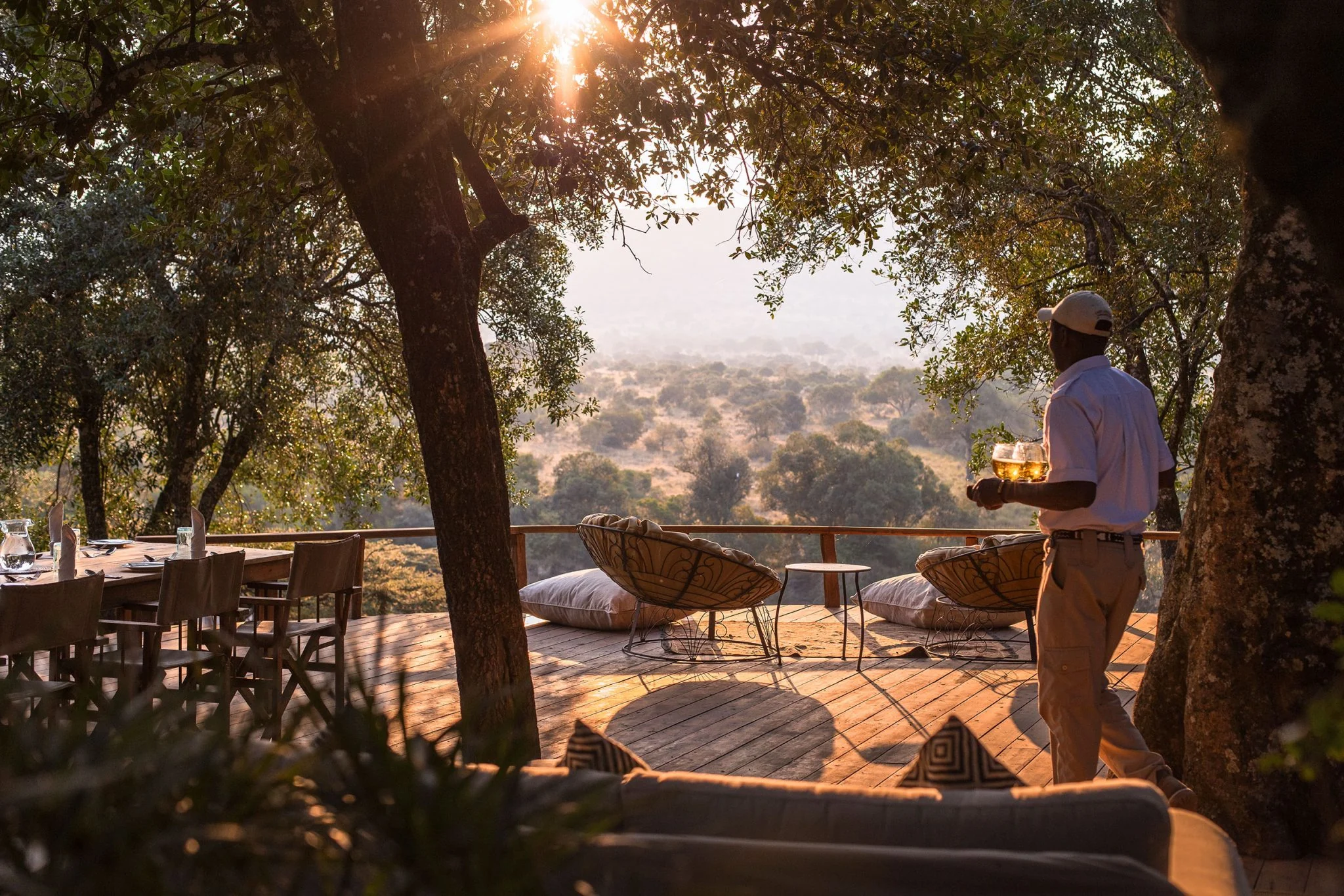 A guide carrying a tray to chairs under the trees at sunset