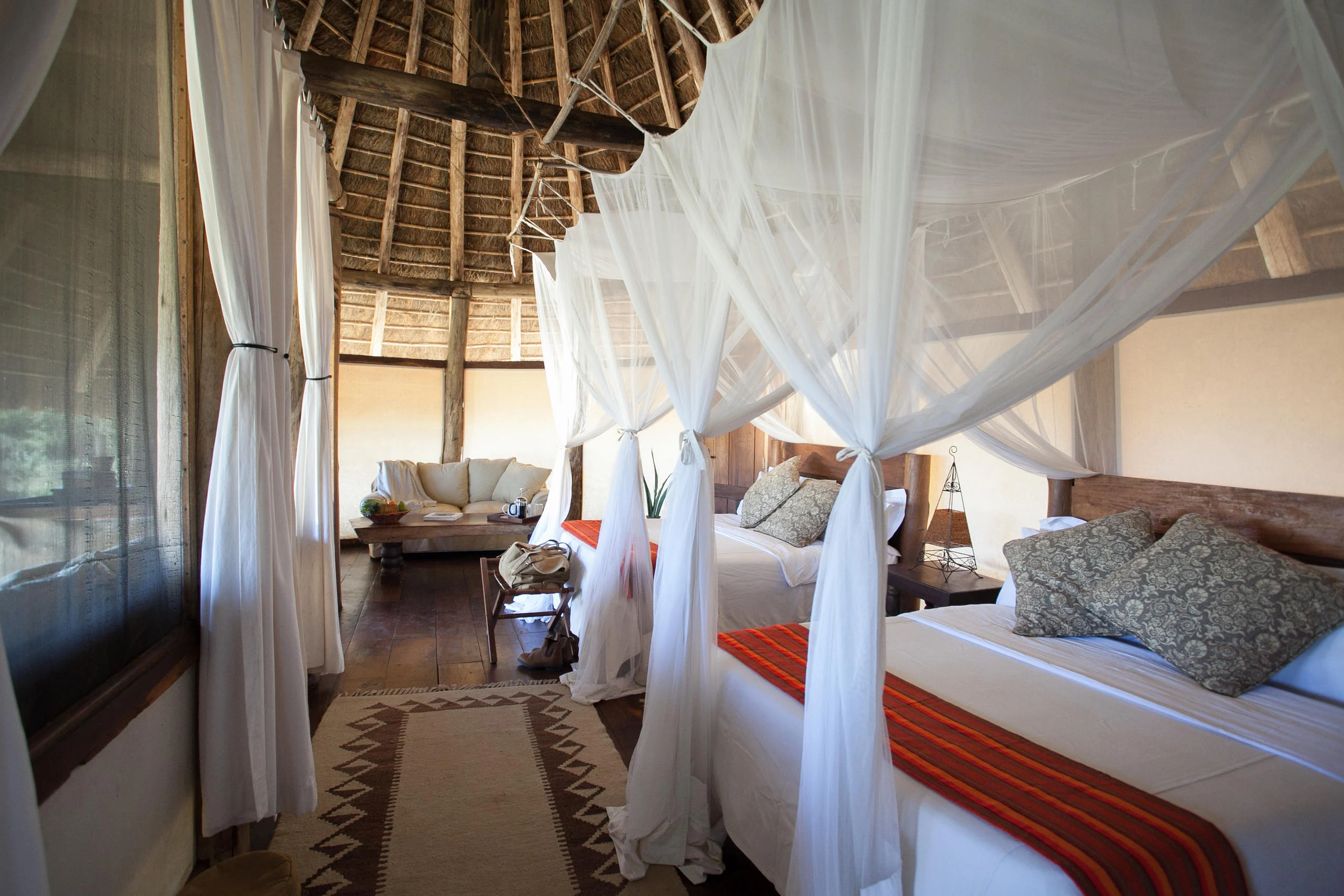 A bedroom with a draped bed under thatch