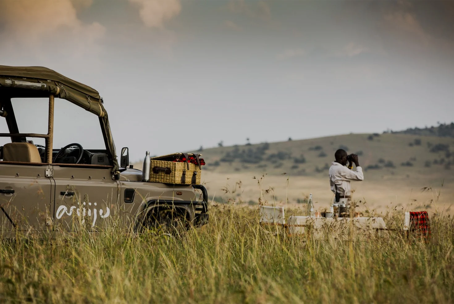 An open vehicle on the plains with a guide standing beyond it