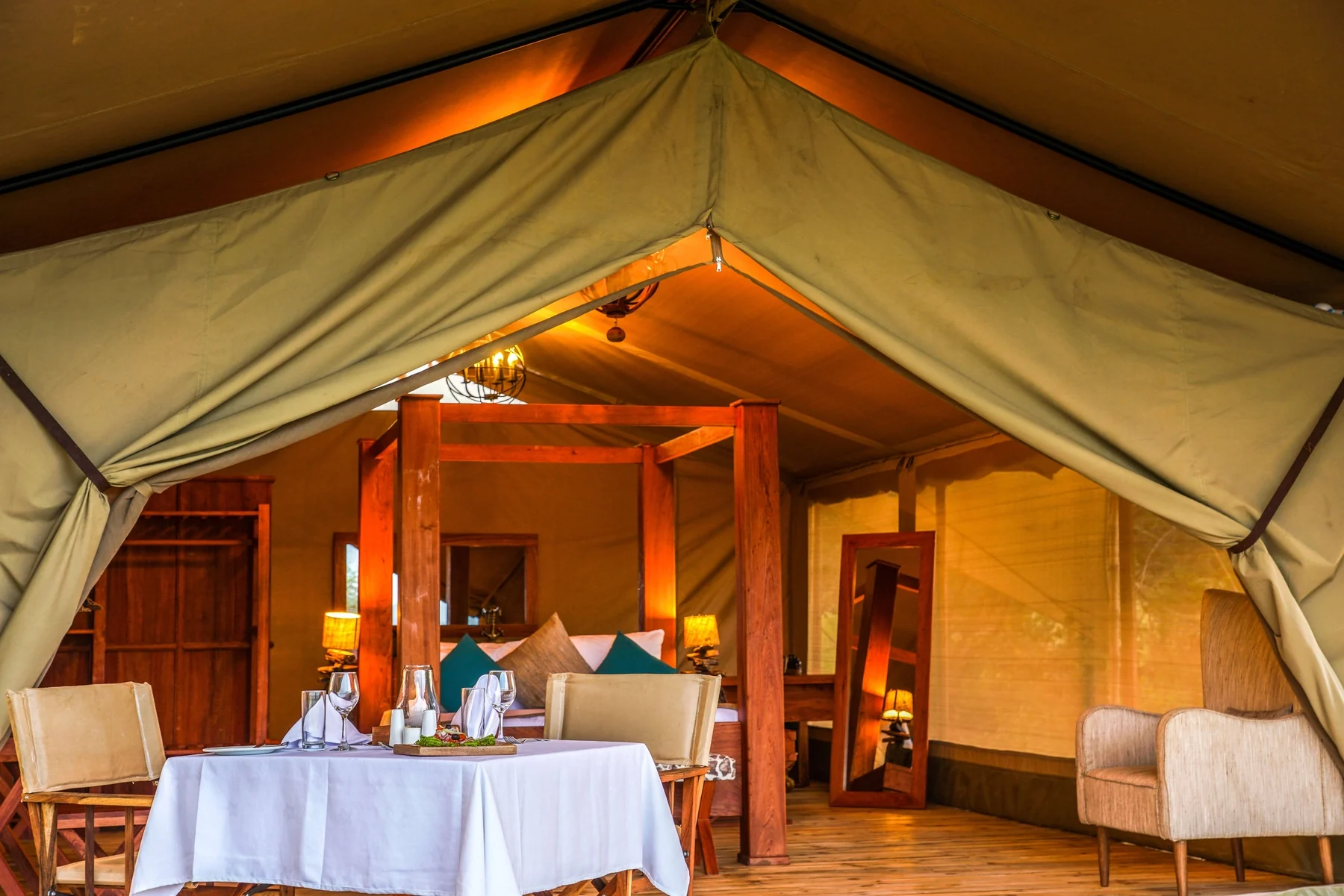 A tent with a table set for dinner at its entrance, lit at dusk