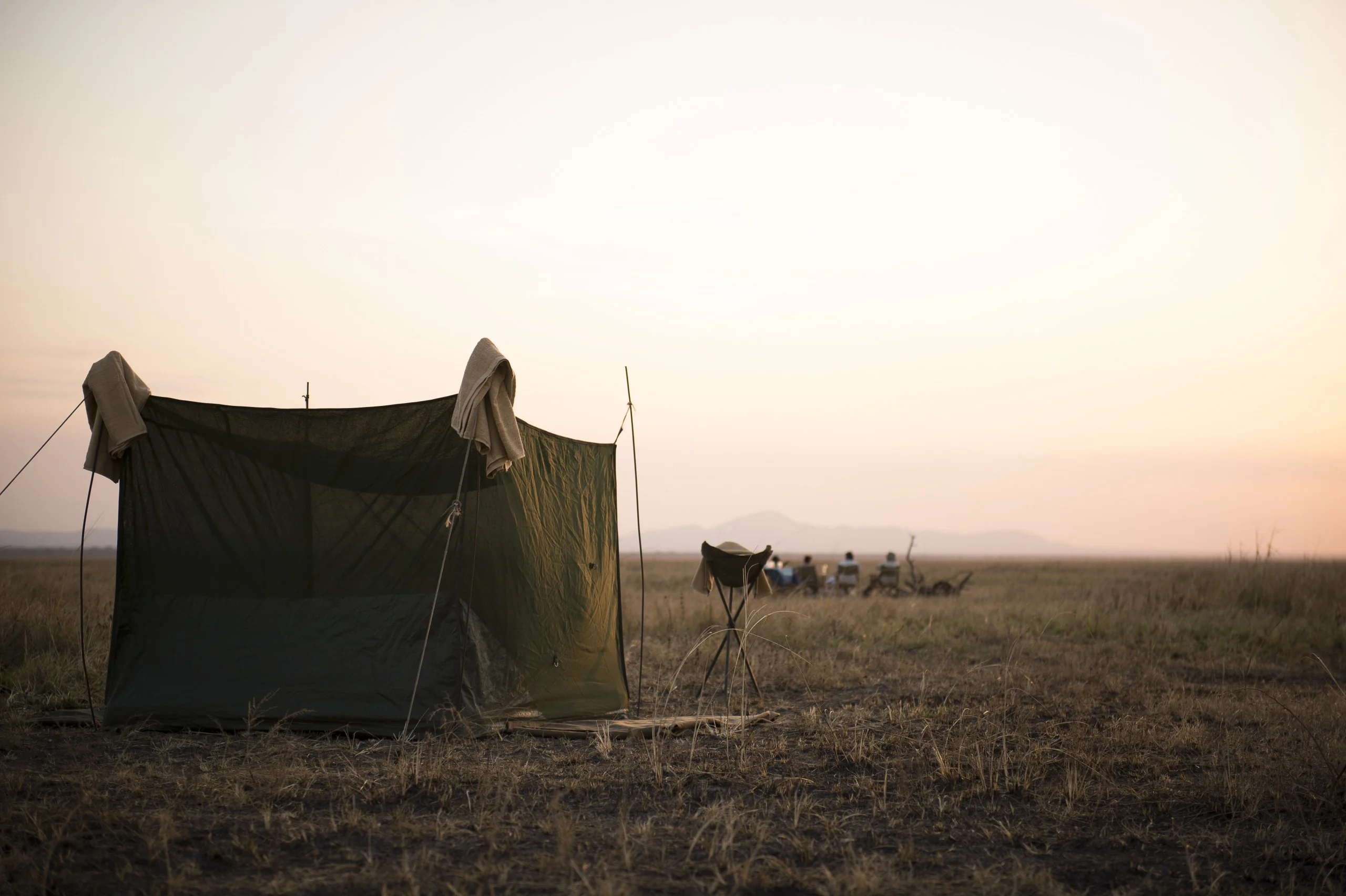 A canvas shower tent on the plains at dusk