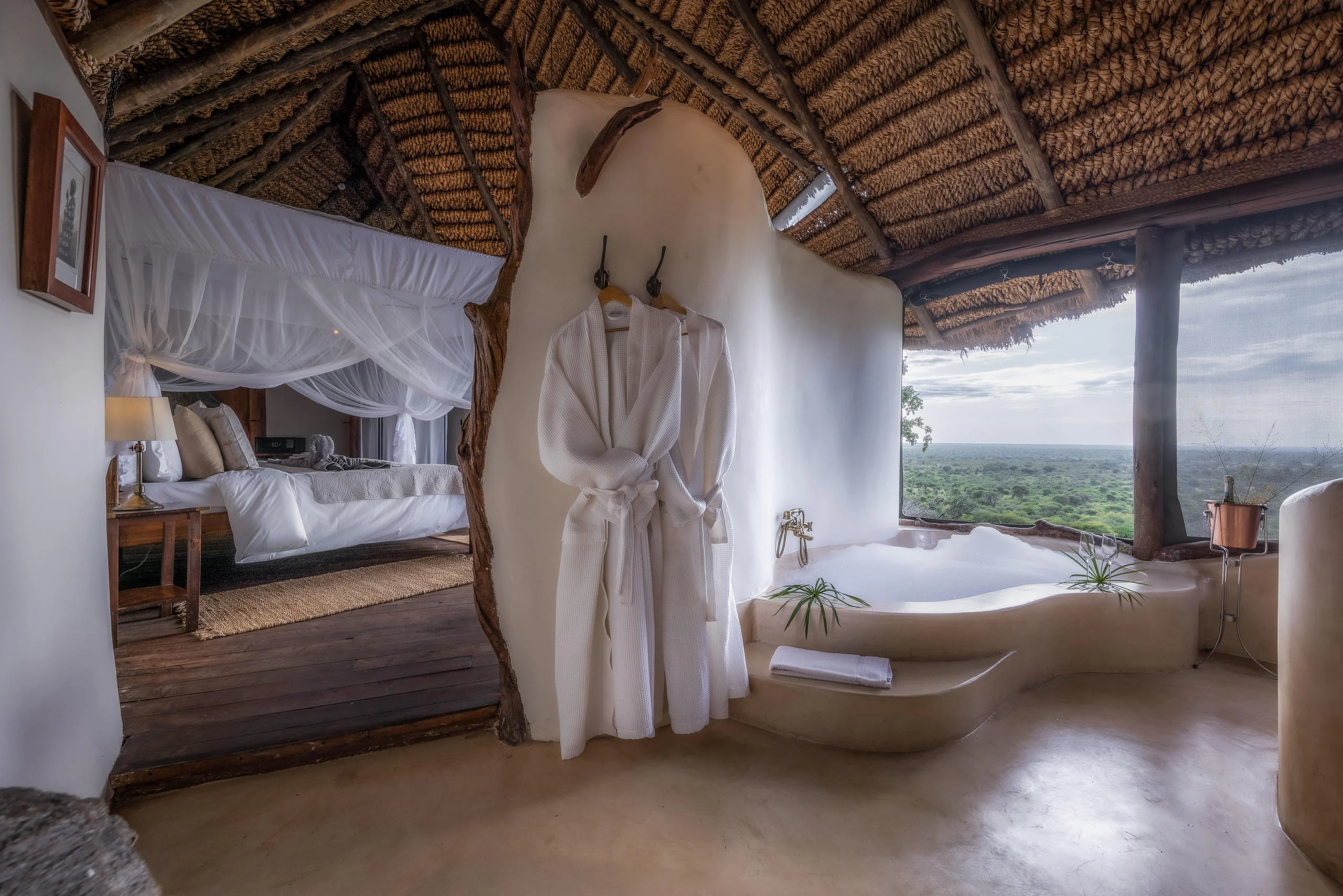 A bathroom with a bath and a draped bed beyond
