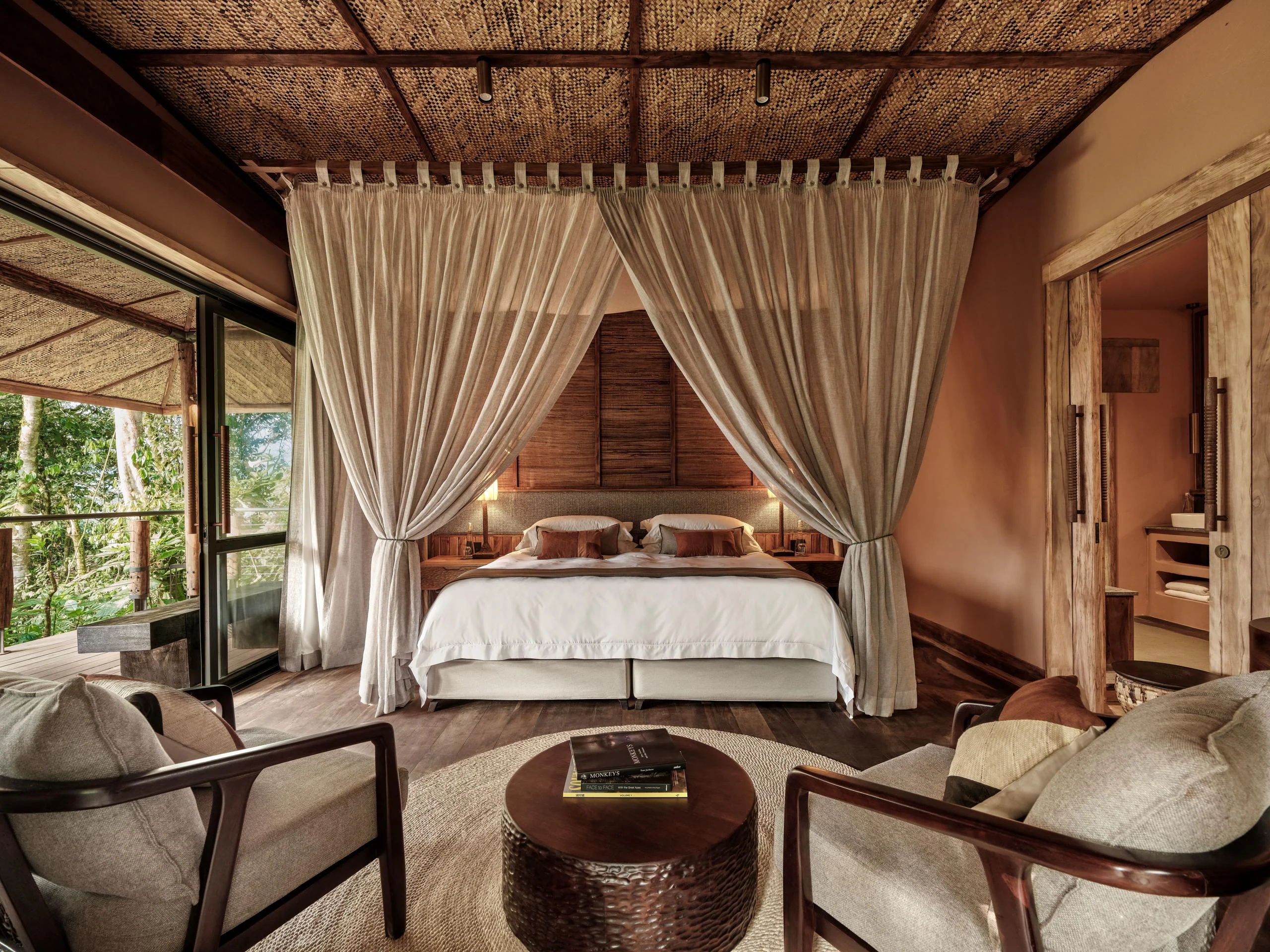 A bedroom with a draped bed and doors onto the forest