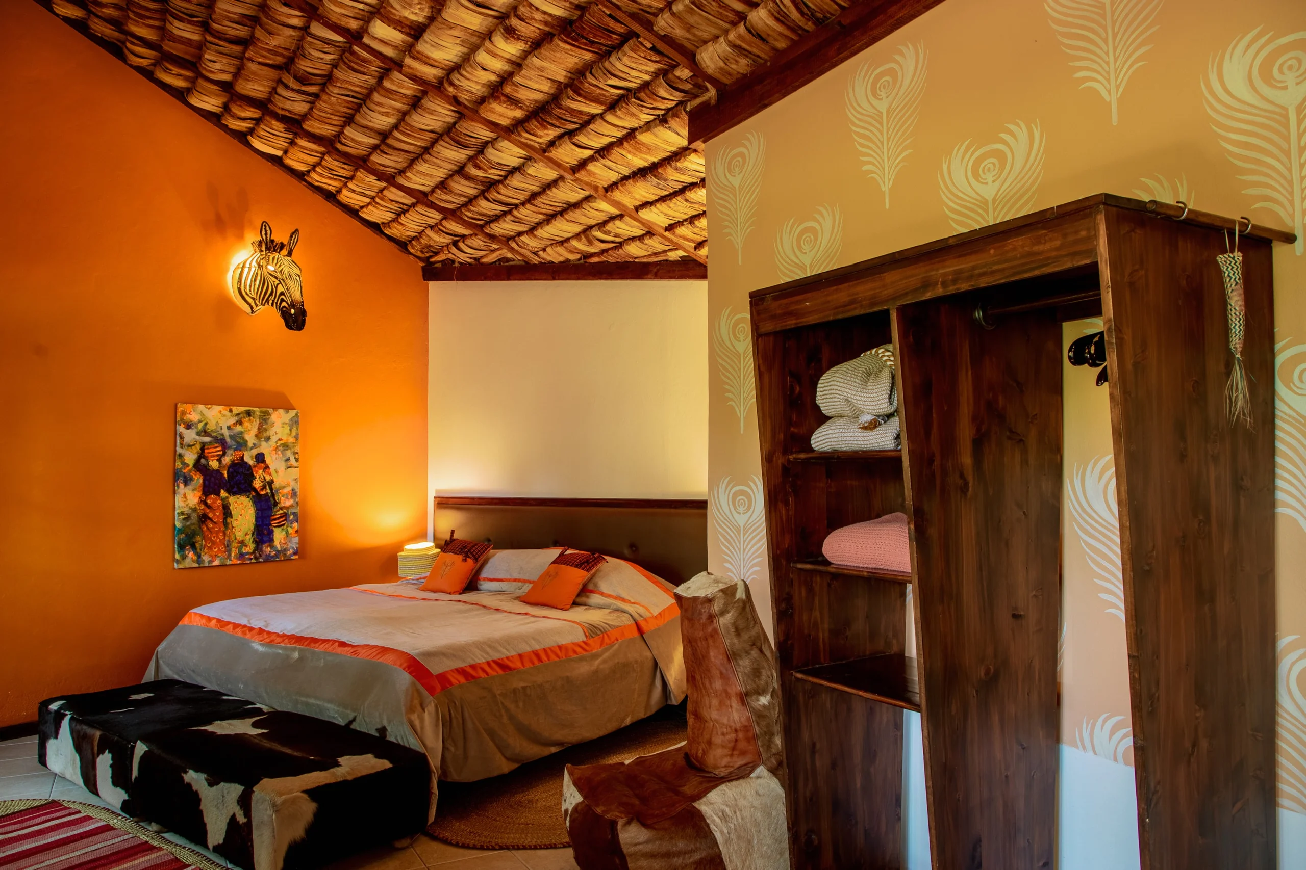 A bedroom with an orange bedspread and a painting on the wall