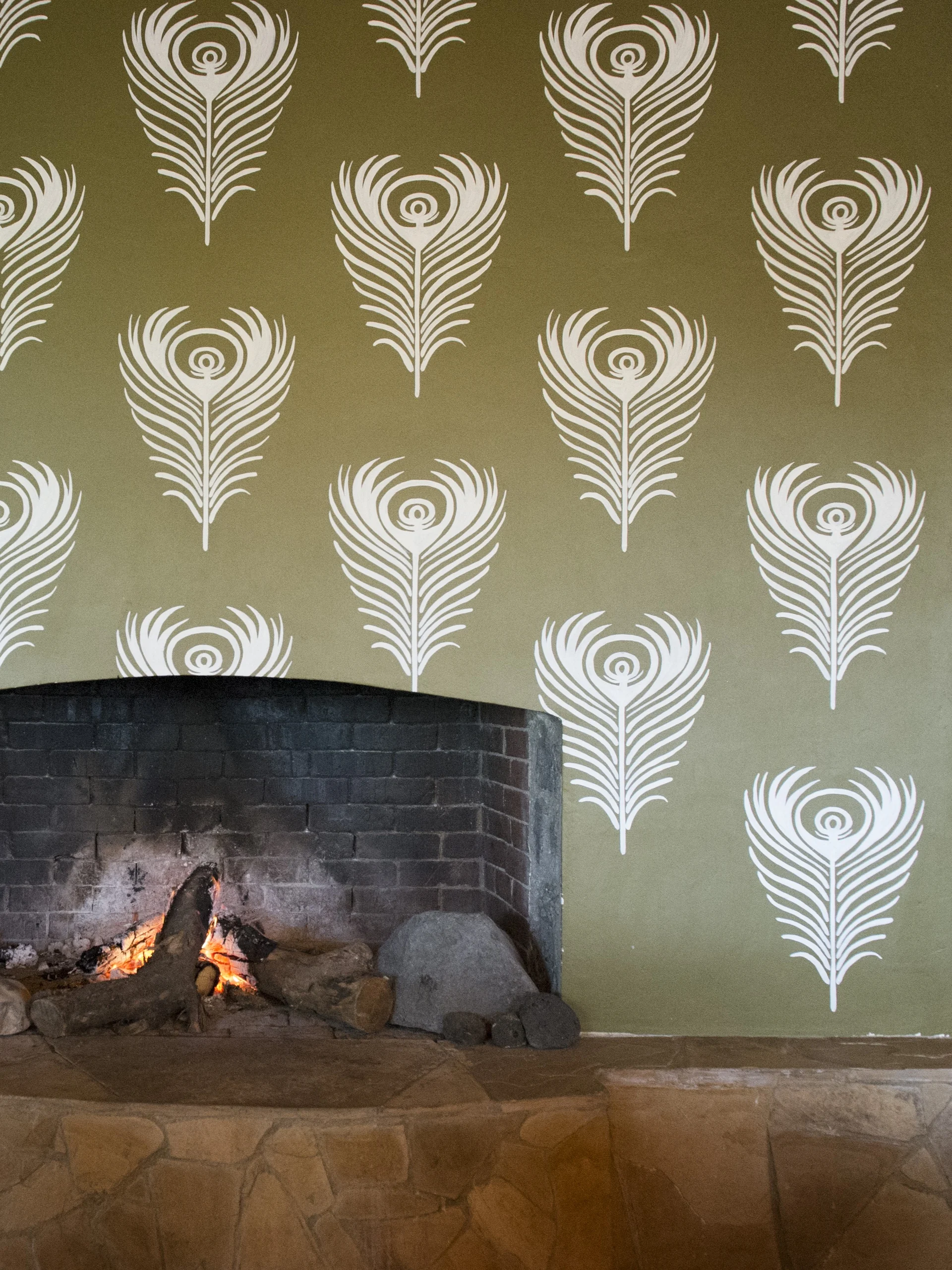 A lit fireplace beneath feather-patterned wallpaper