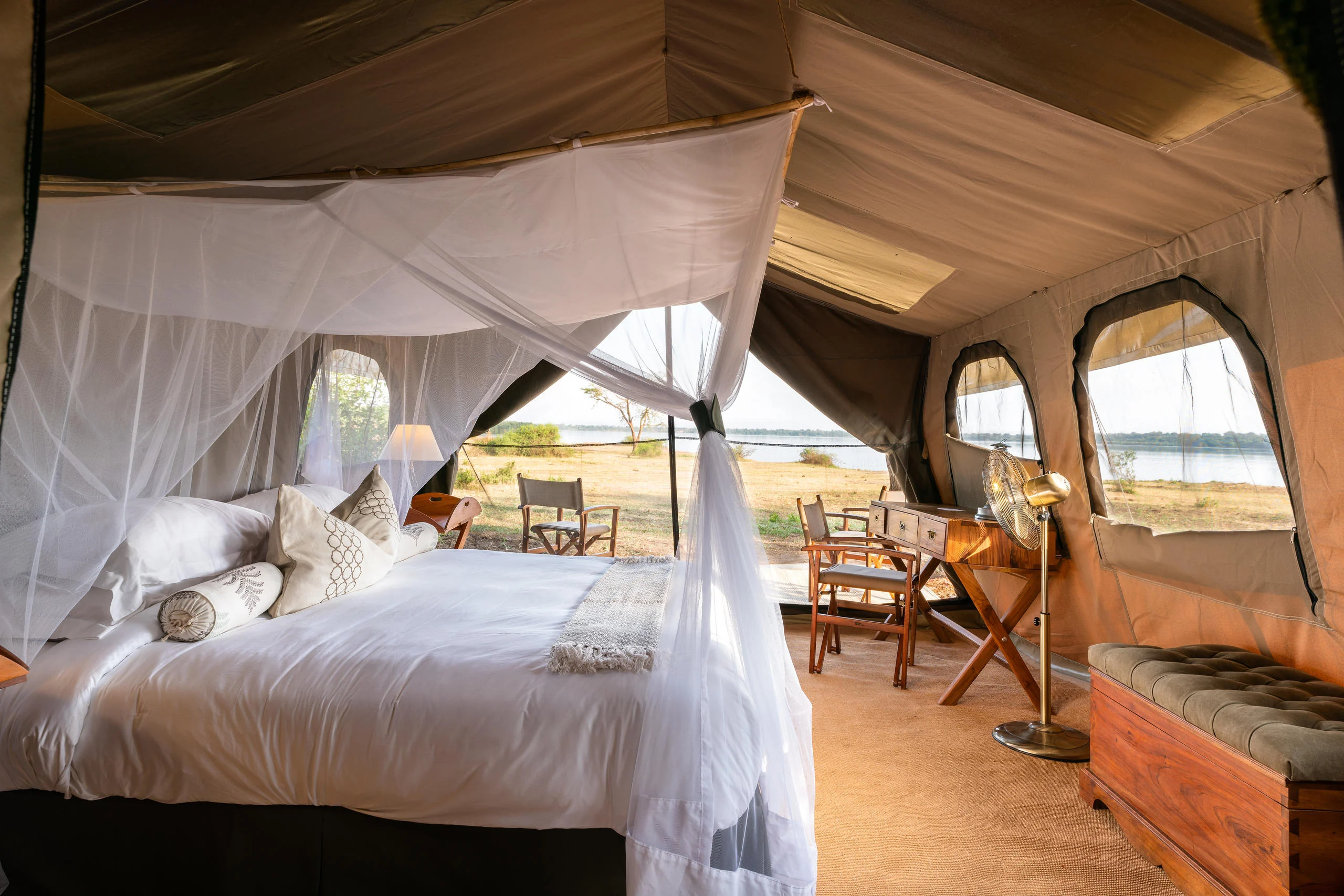 A tent bedroom with a draped bed and the lake beyond