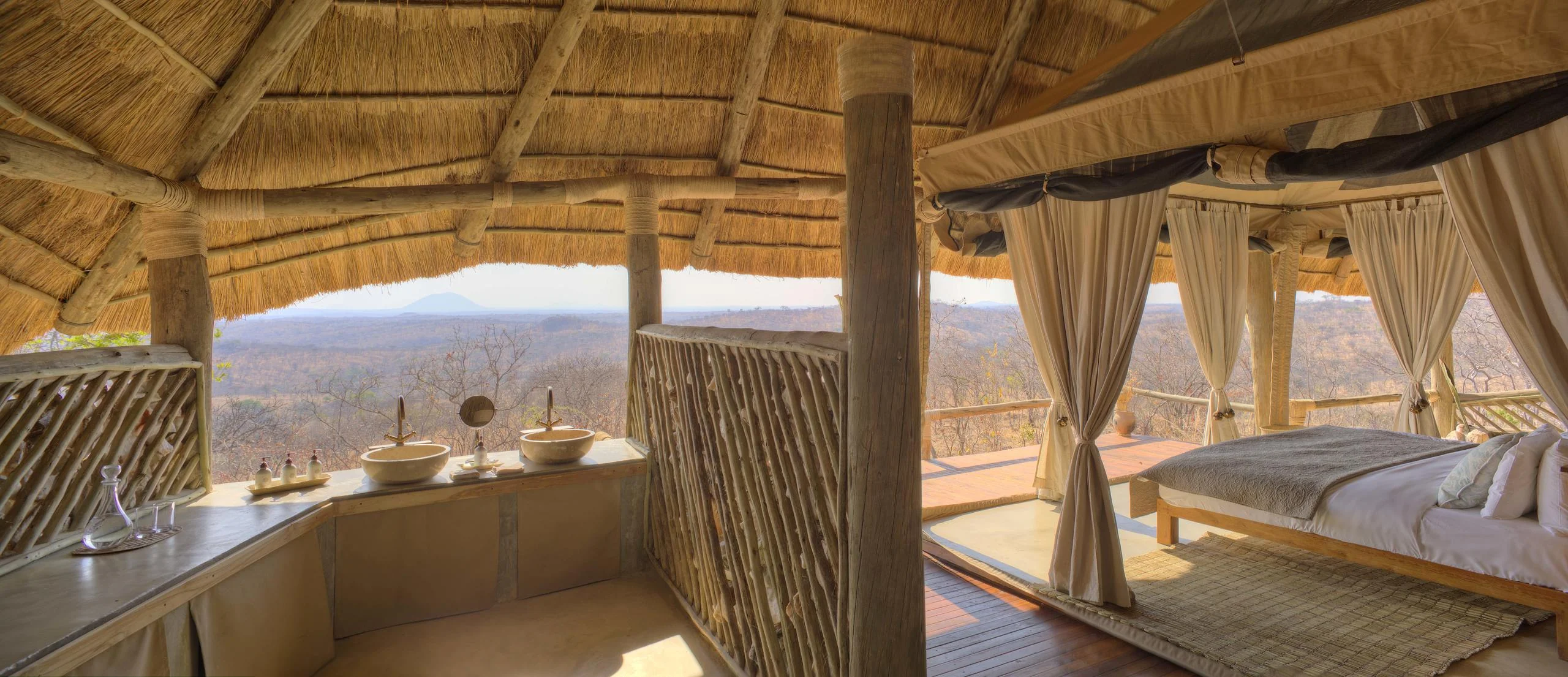 A thatched guest room with the bed facing the open front and the view