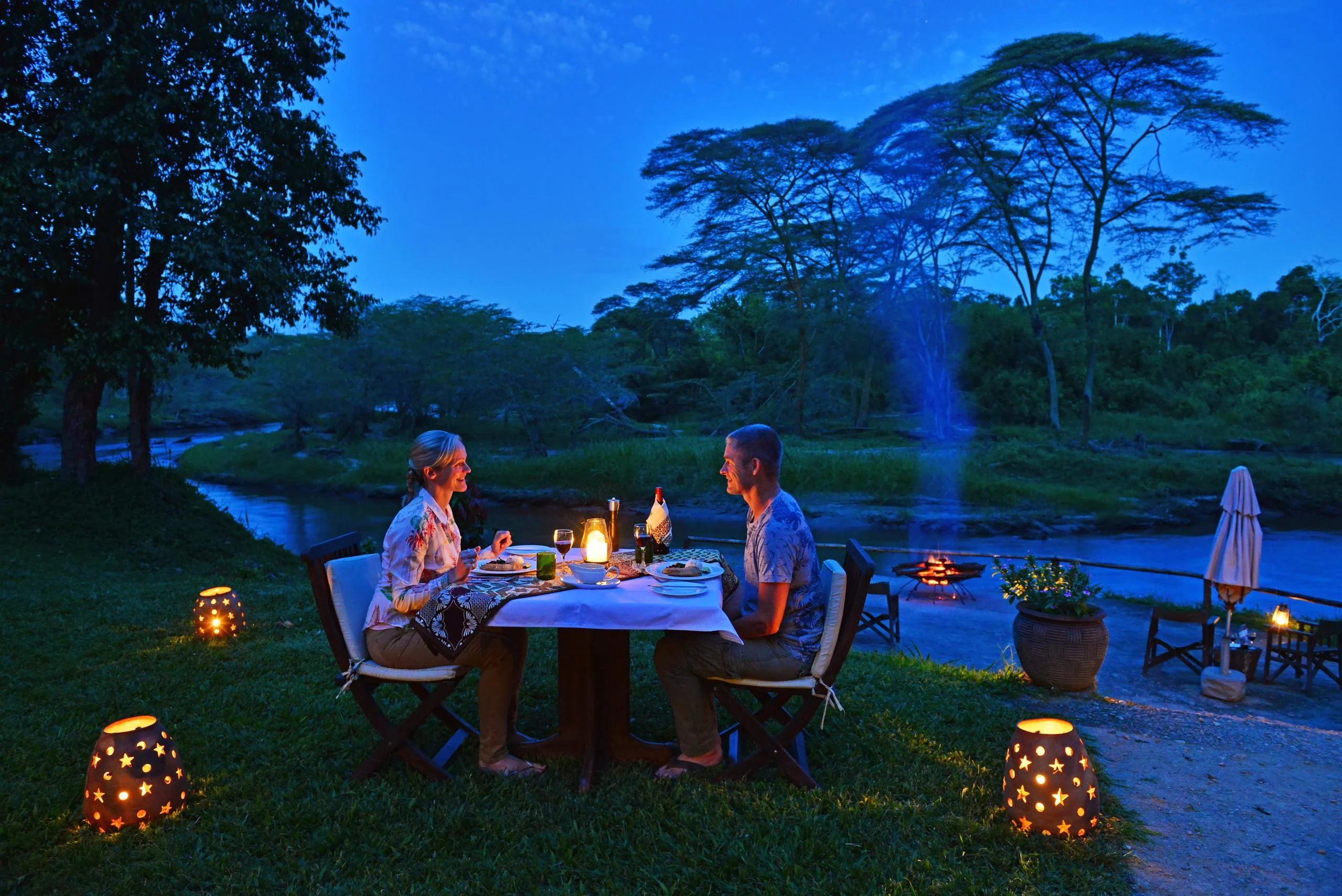Two guests at dinner beside the river, lit by lanterns
